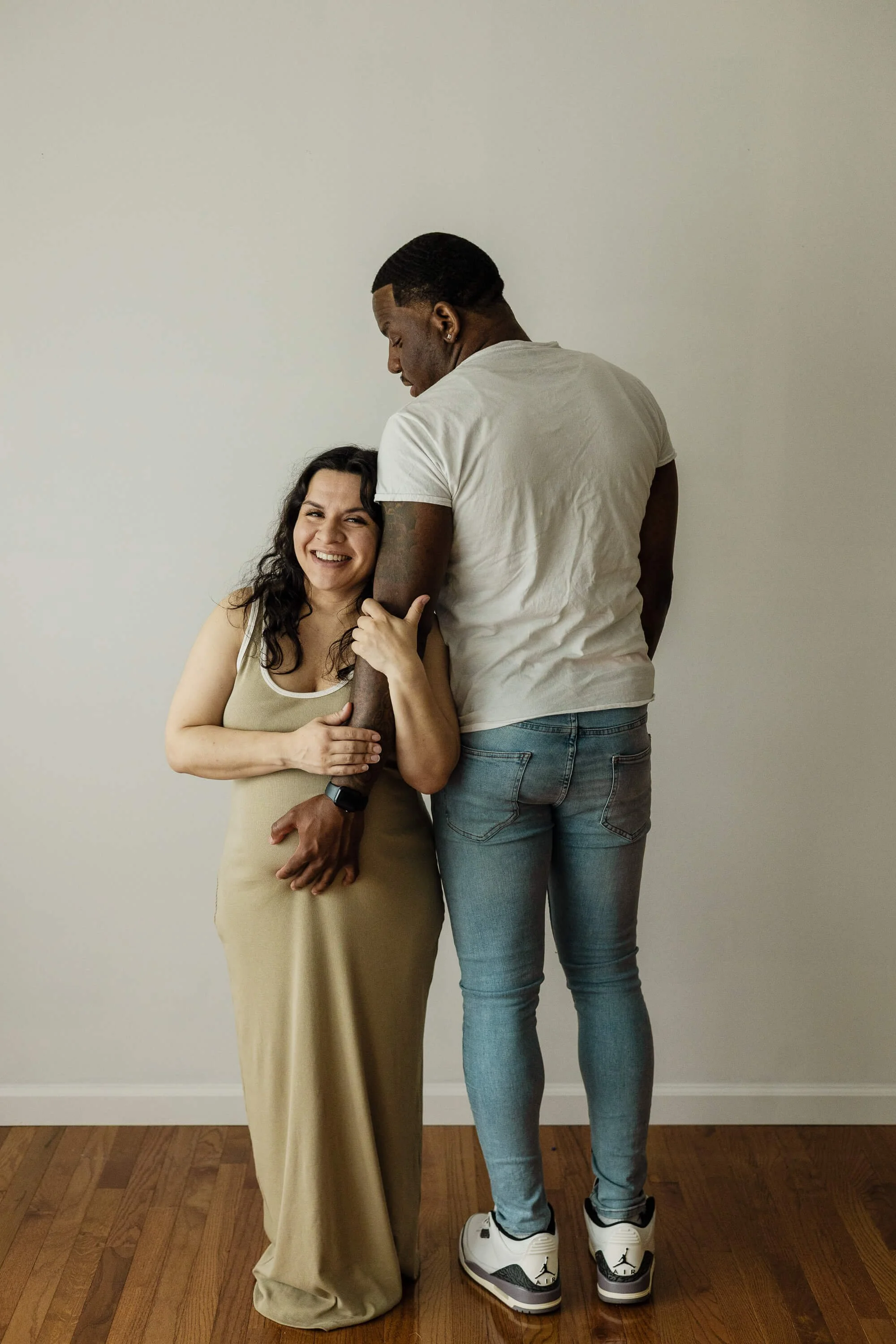 A couple poses, the man's hand enveloping her pregnant belly while she smiles 
