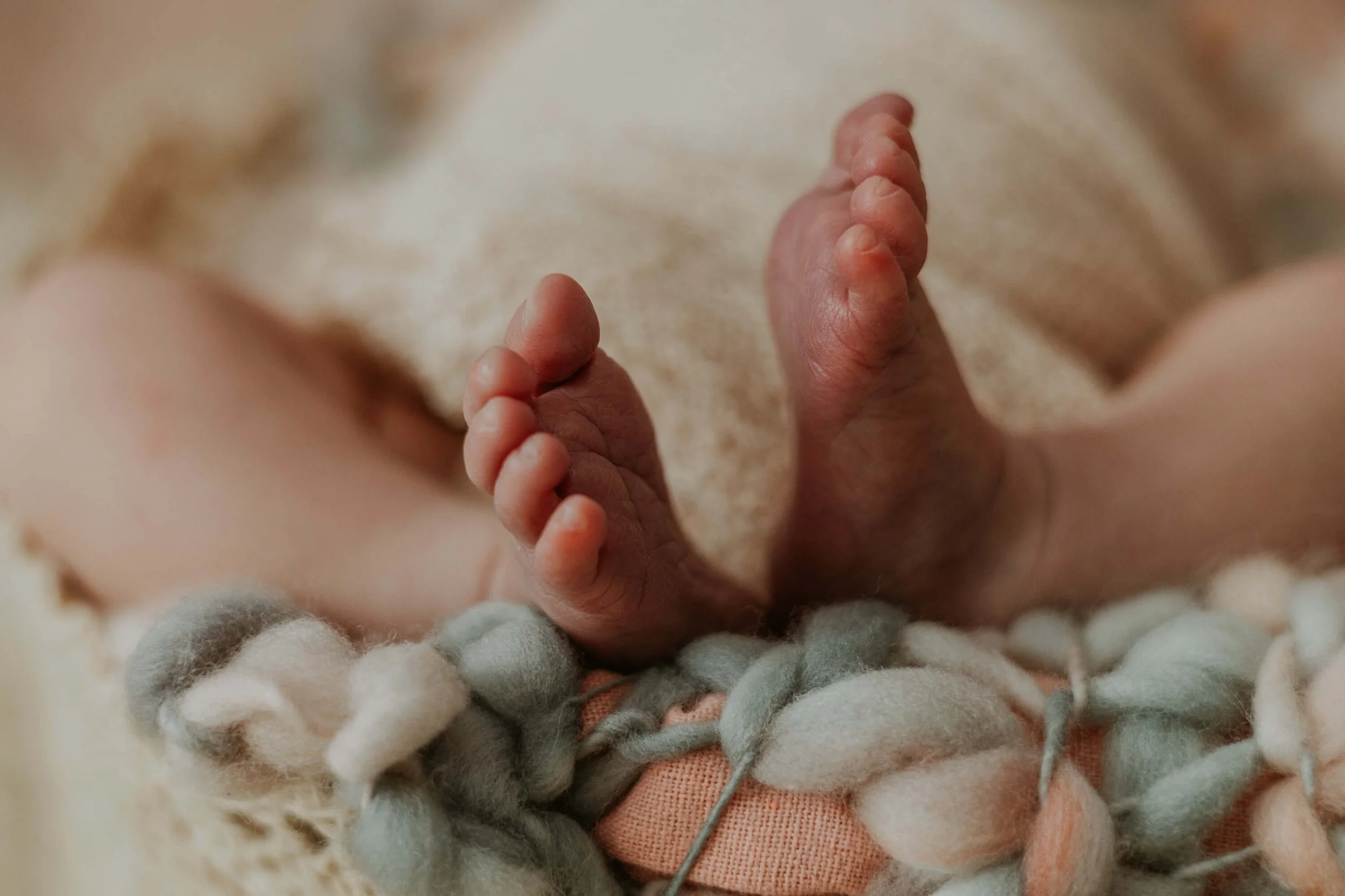Newborn toes peeking out of a swaddle atop a woven blanket