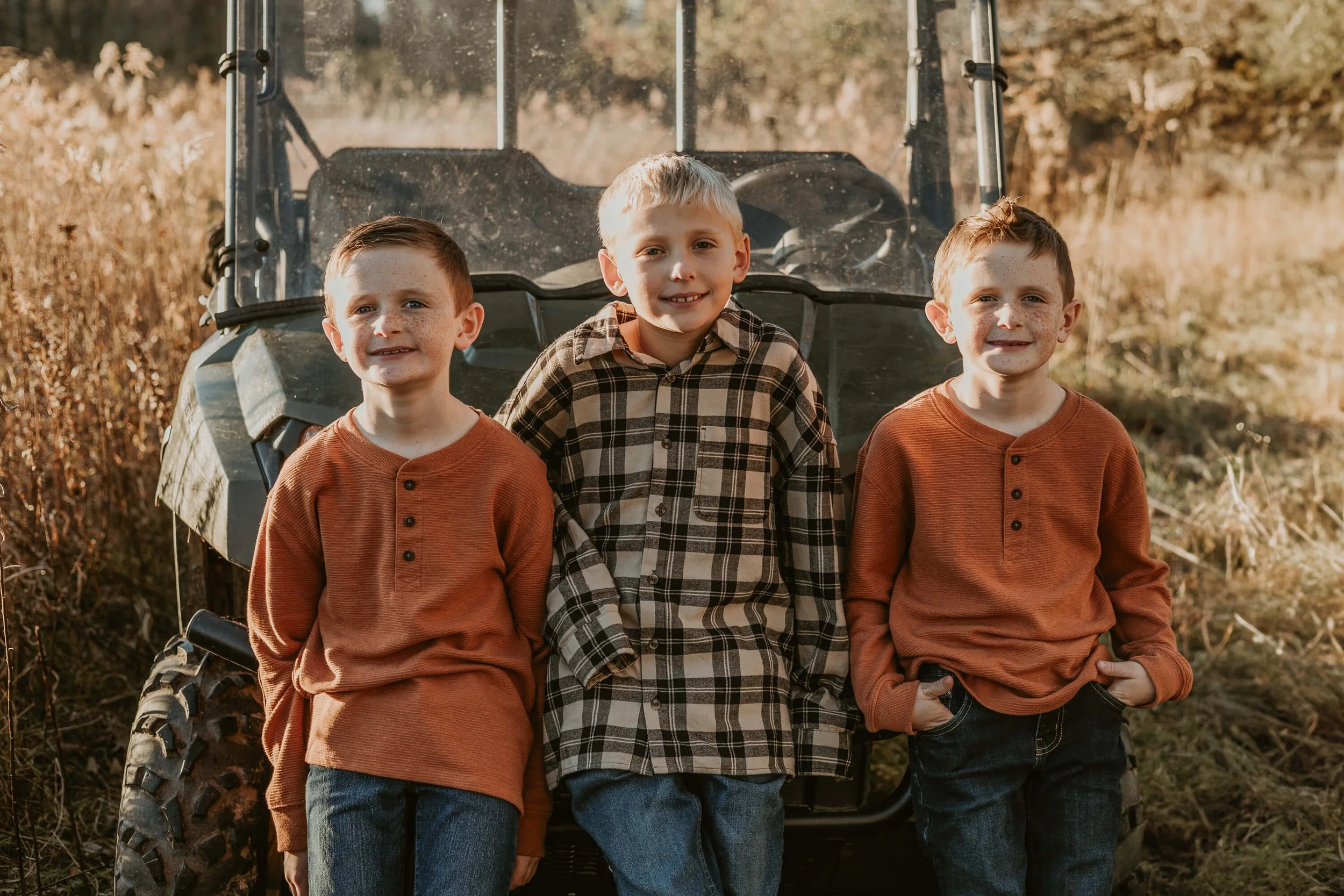 Three young brothers lean against a golf cart while exploring their family property outside of Bloomington IL