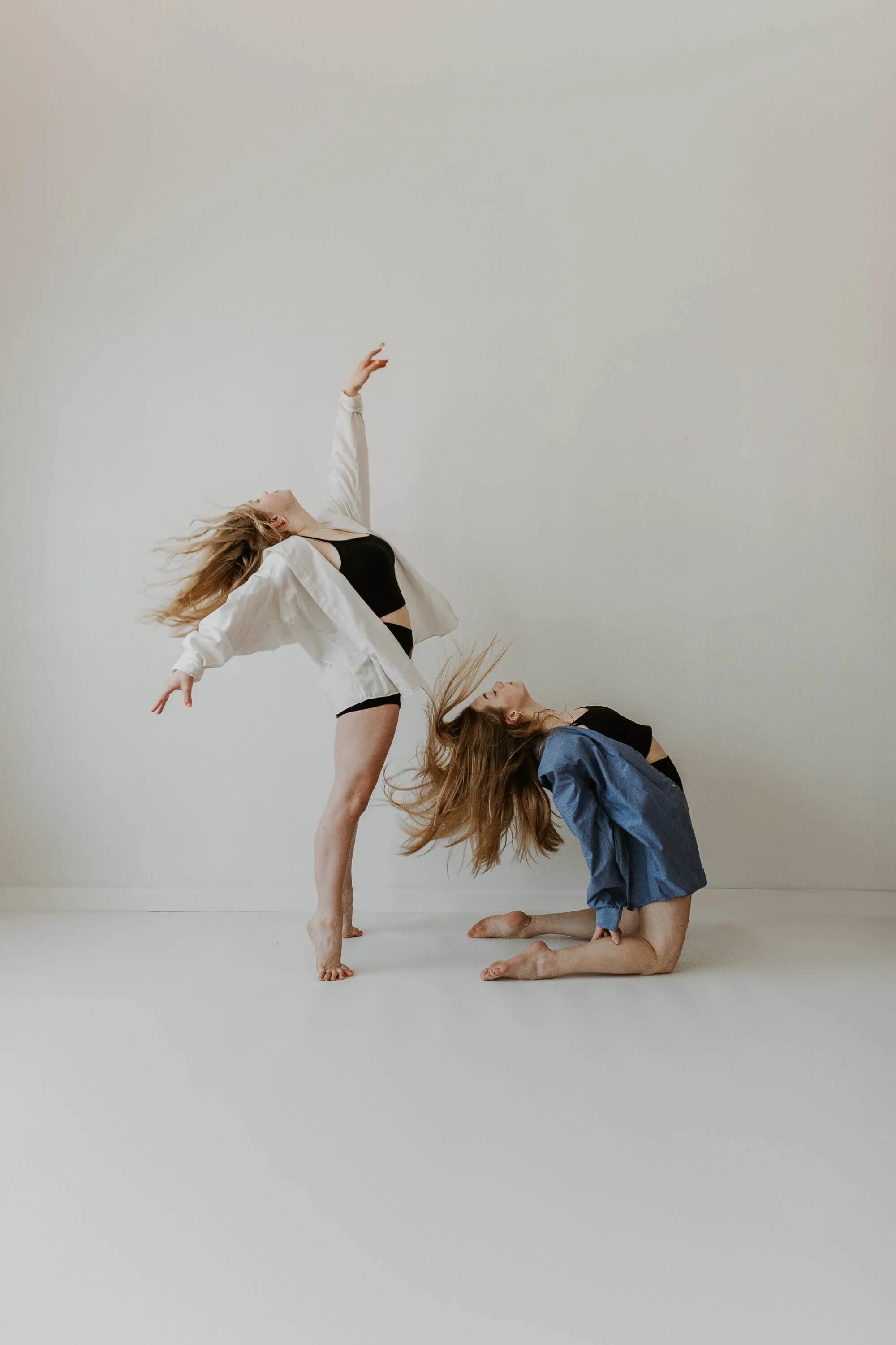 Two dancers, one kneeling, the other behind is standing, throw their heads back simeltaneously, their hair arching backwards.