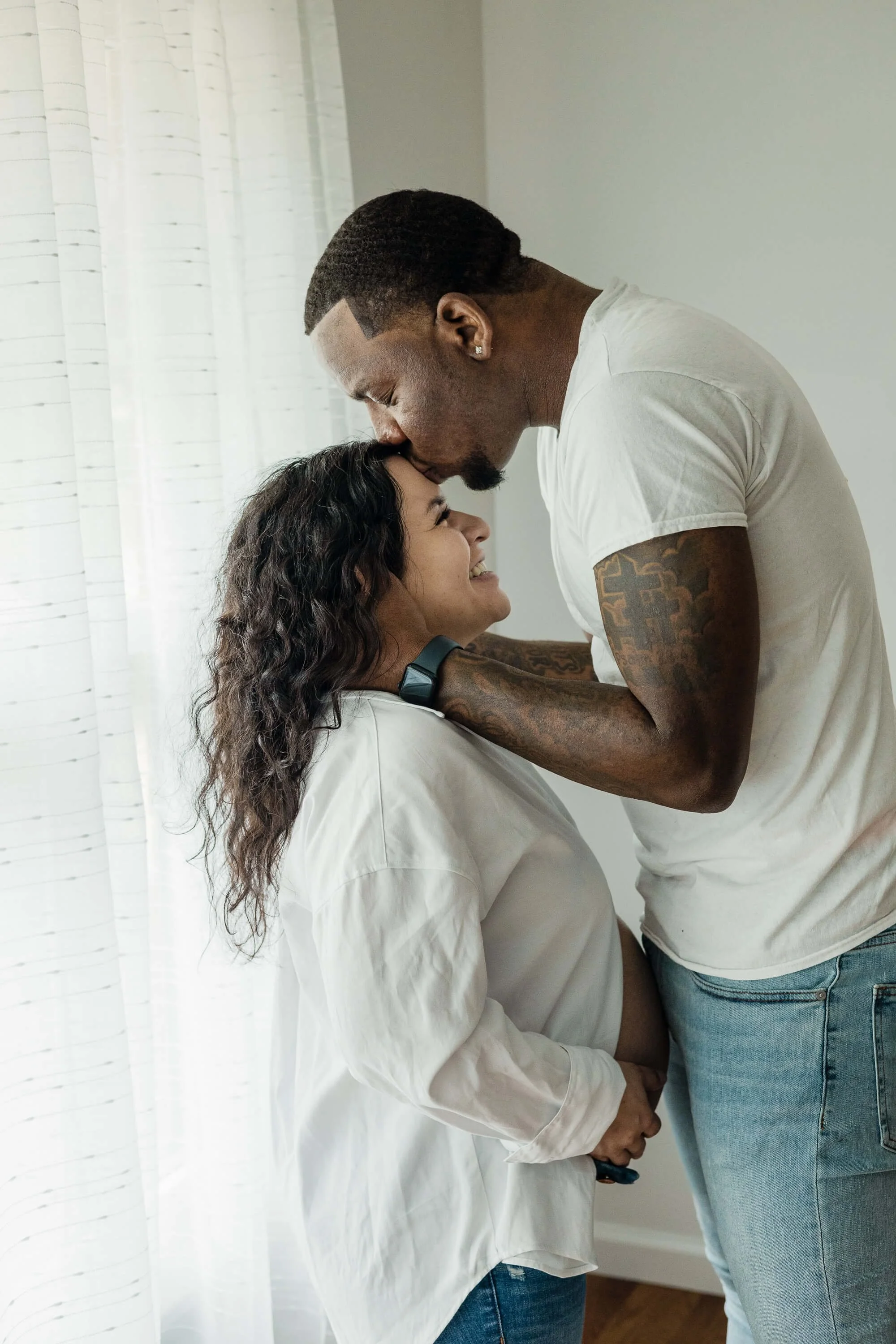 A dad-to-be plants a soft kiss on his partner's forehead