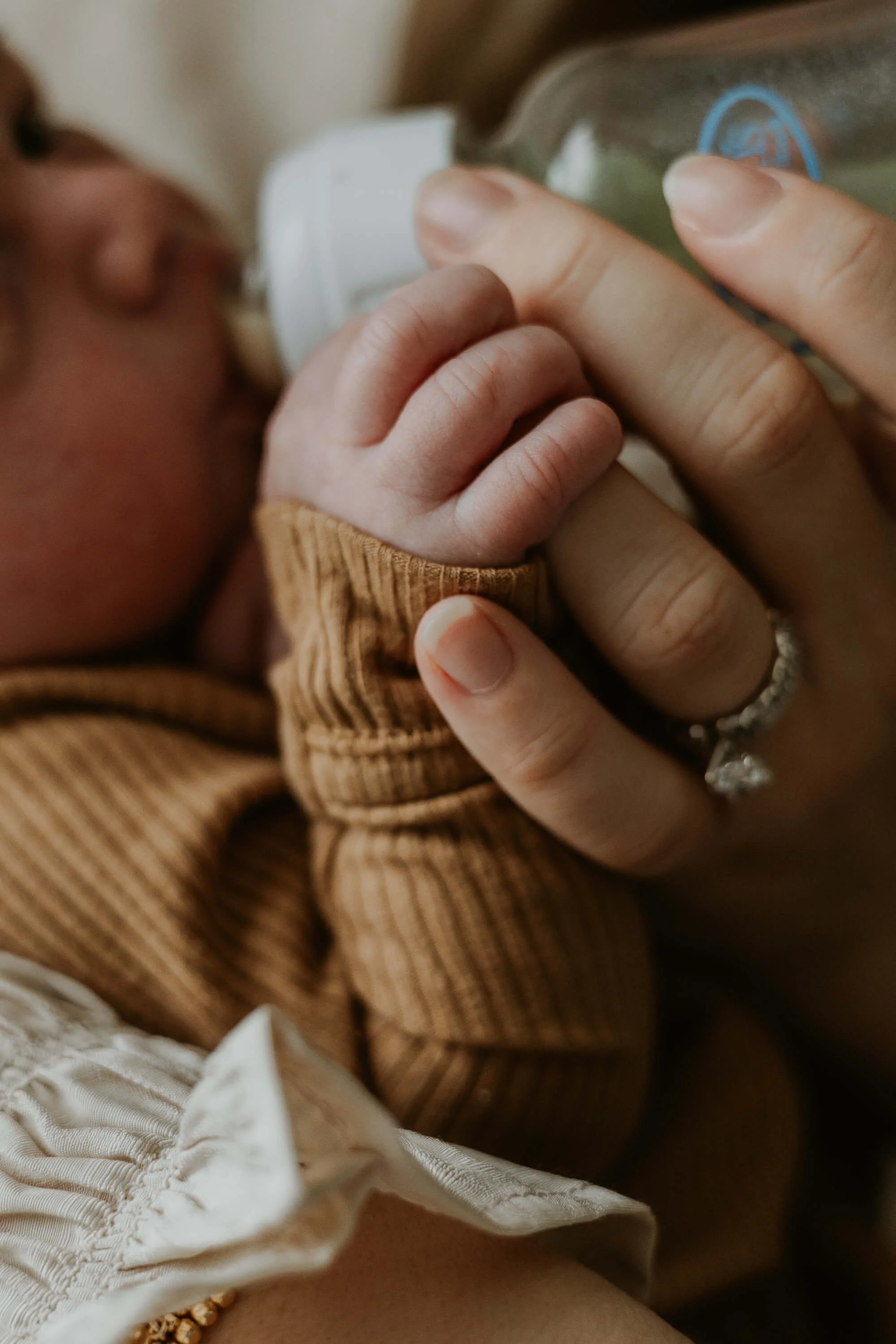 A close up of a mother bottle feeding her son as his fingers tightly grasp her ring finger