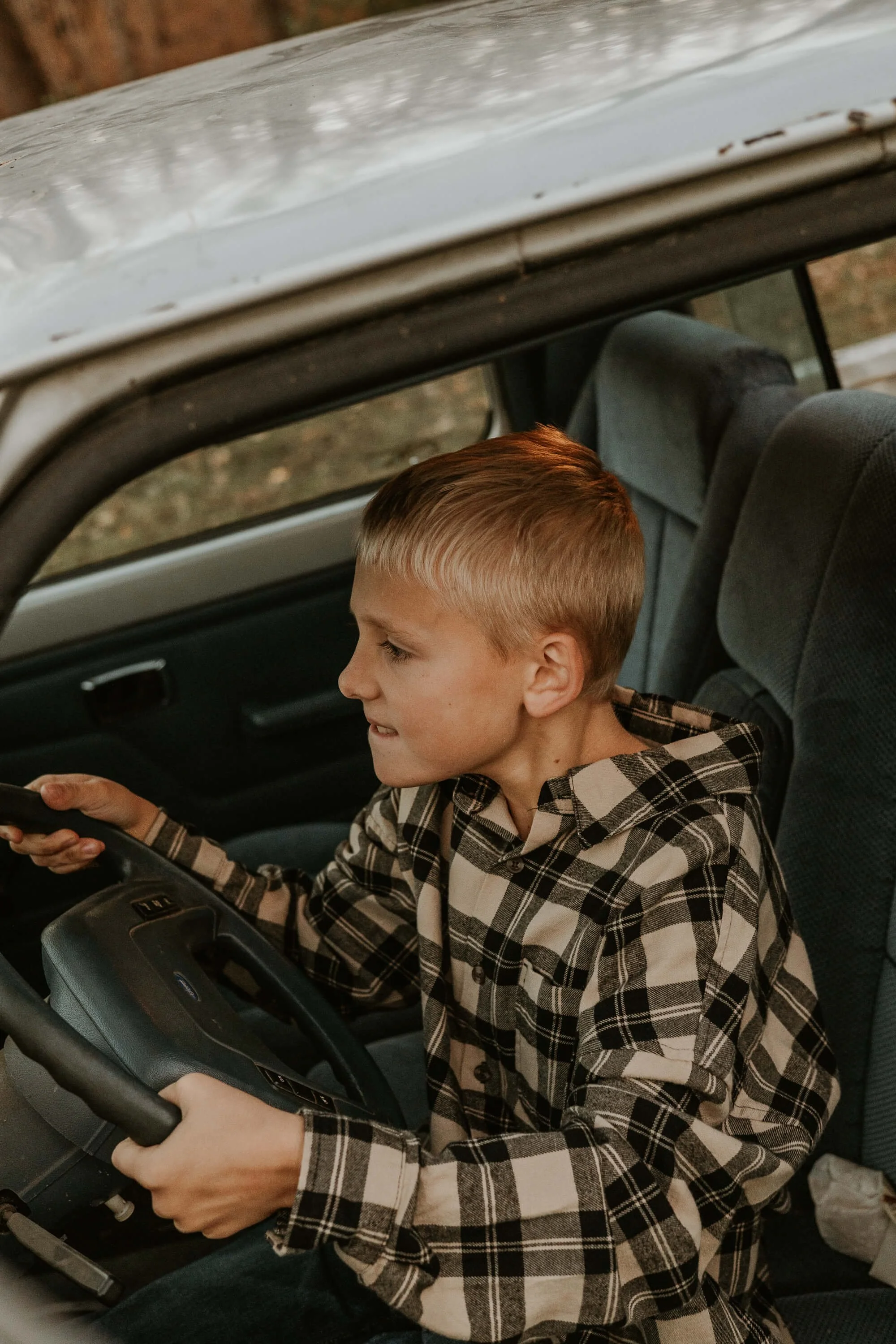 A ten year old boy pretends to race as he sits behind the wheel of an old vehicle