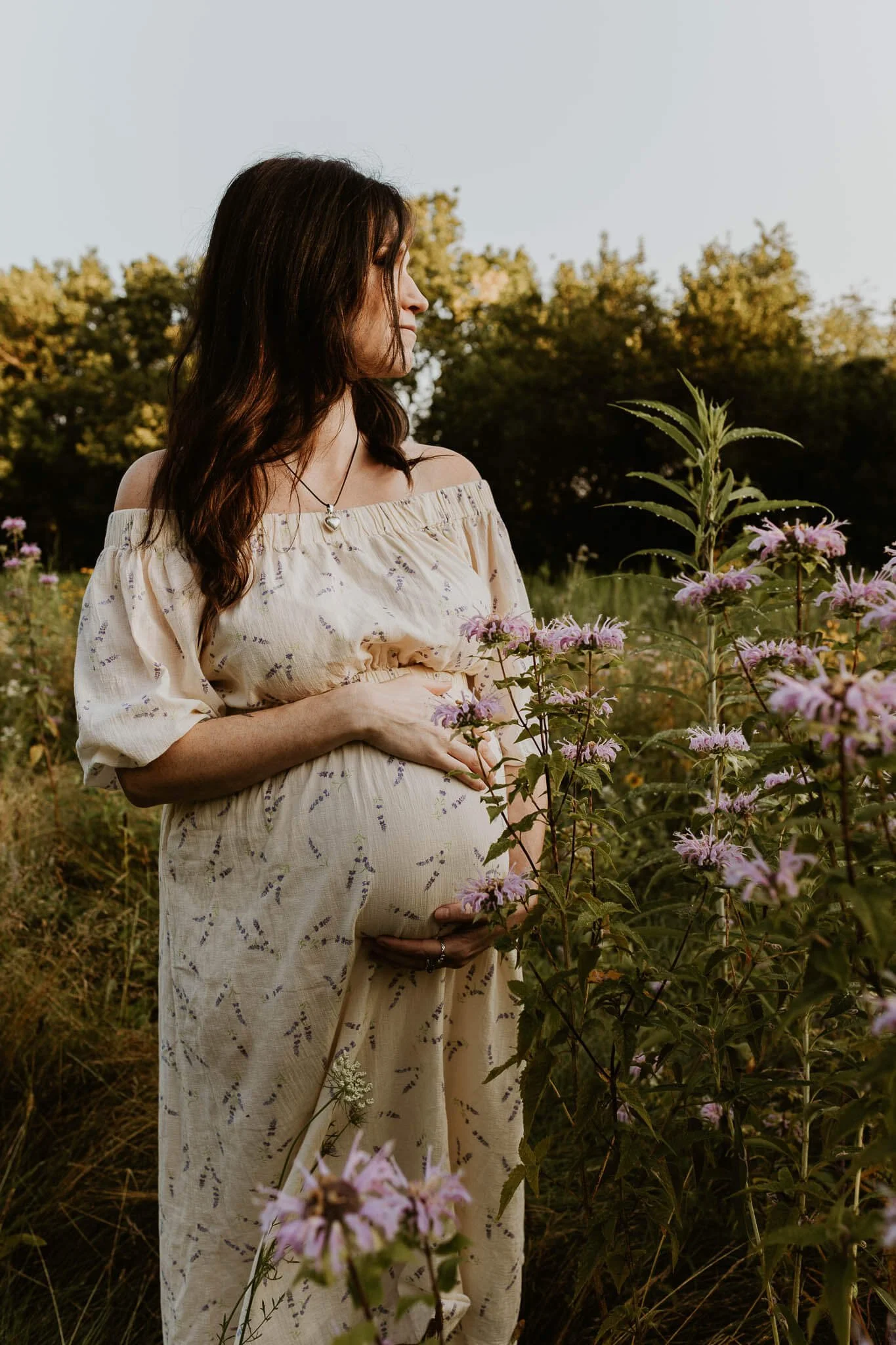 A woman gently holds her pregnant belly amongst wildflowers at a local park