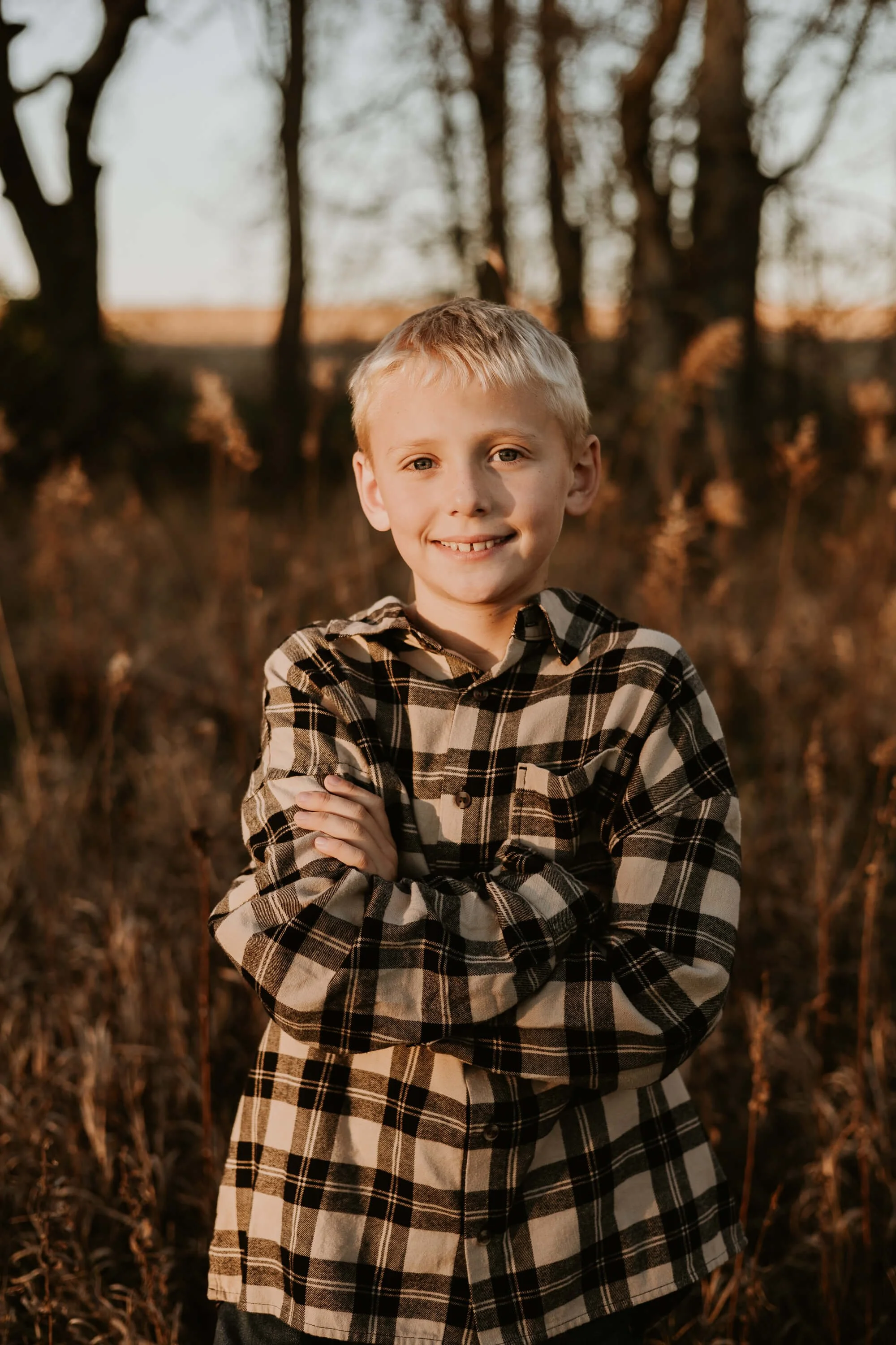 A ten year old boy grins with his arms crossed while the sun sets just to the west