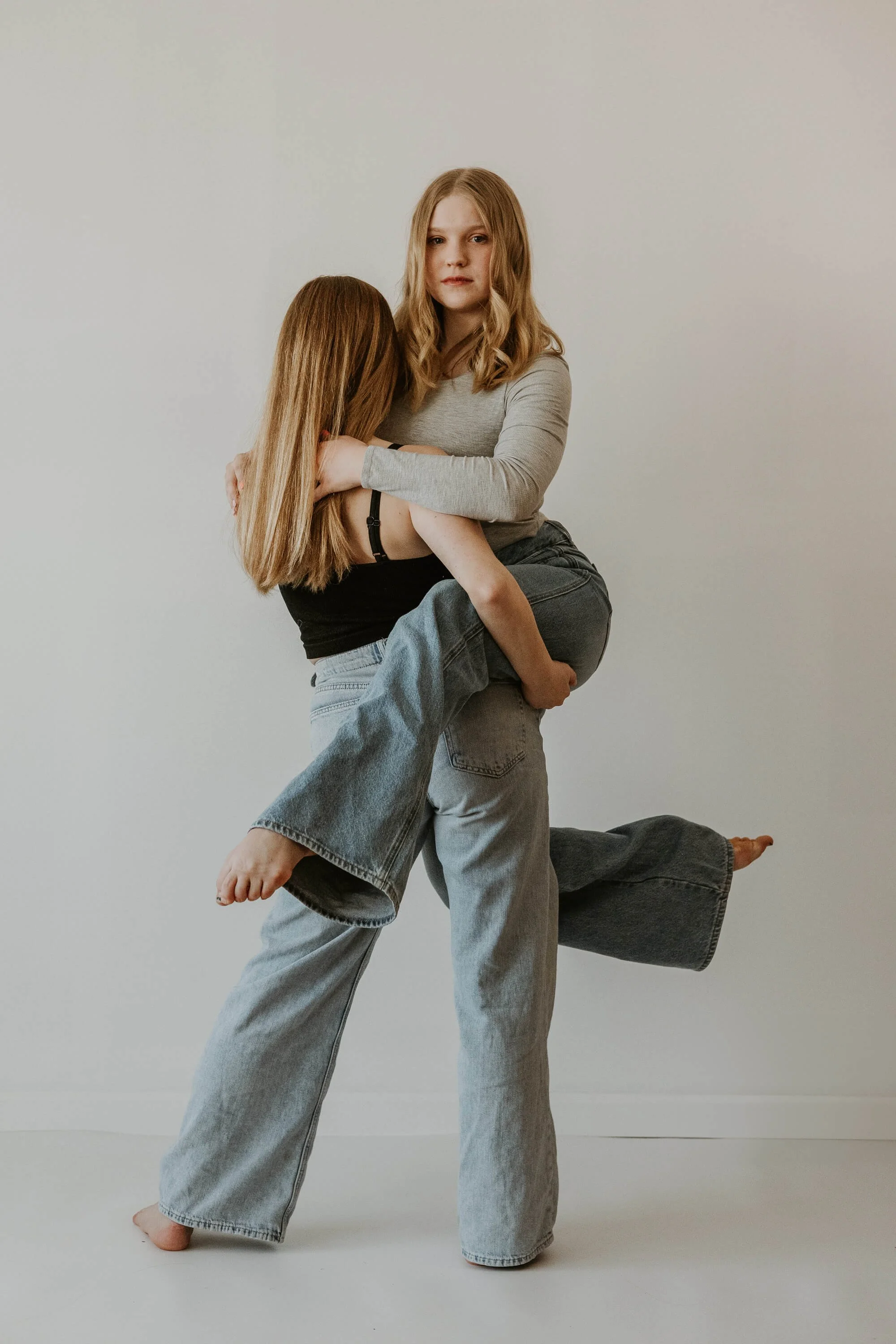 Two ballet dancers dressed casually in jeans, one with her back to the camera holds the other who seemlessly points her toes in a graceful stance.