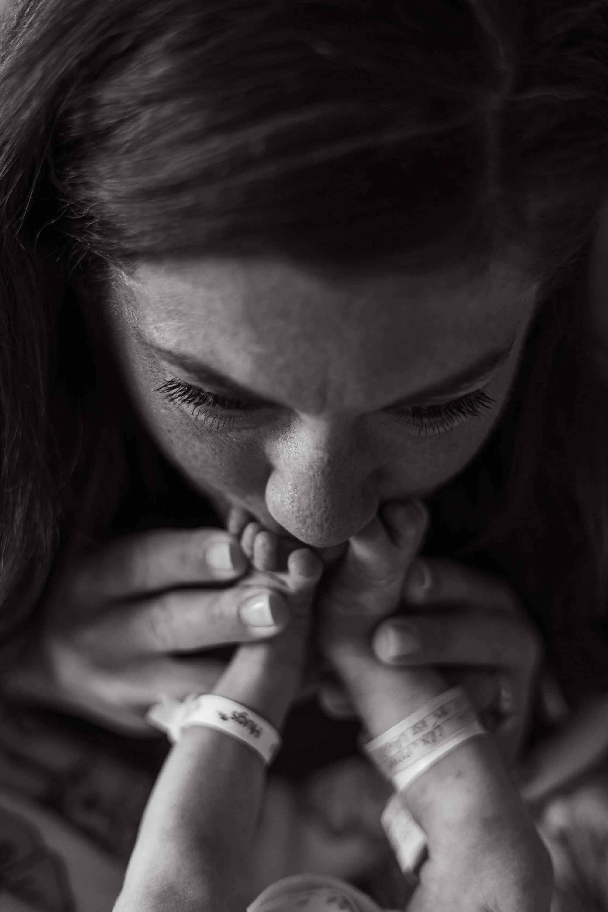 A black and white close up of a mother giving her newborn's feet kisses