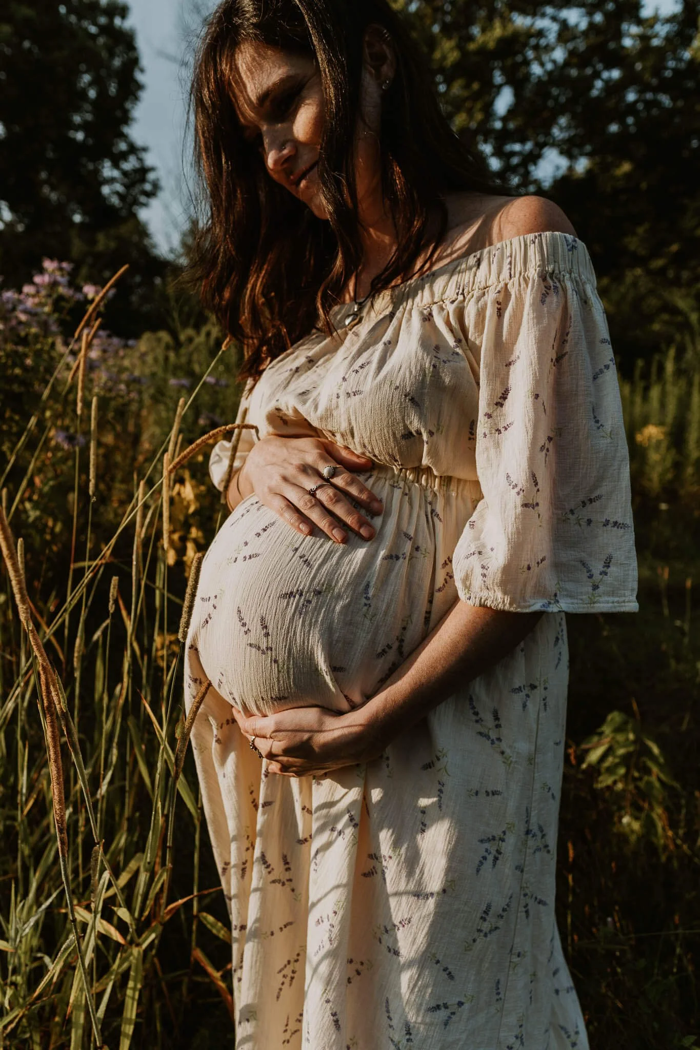 A pregnant mom dressed in a floral print dress tenderly hugs her belly