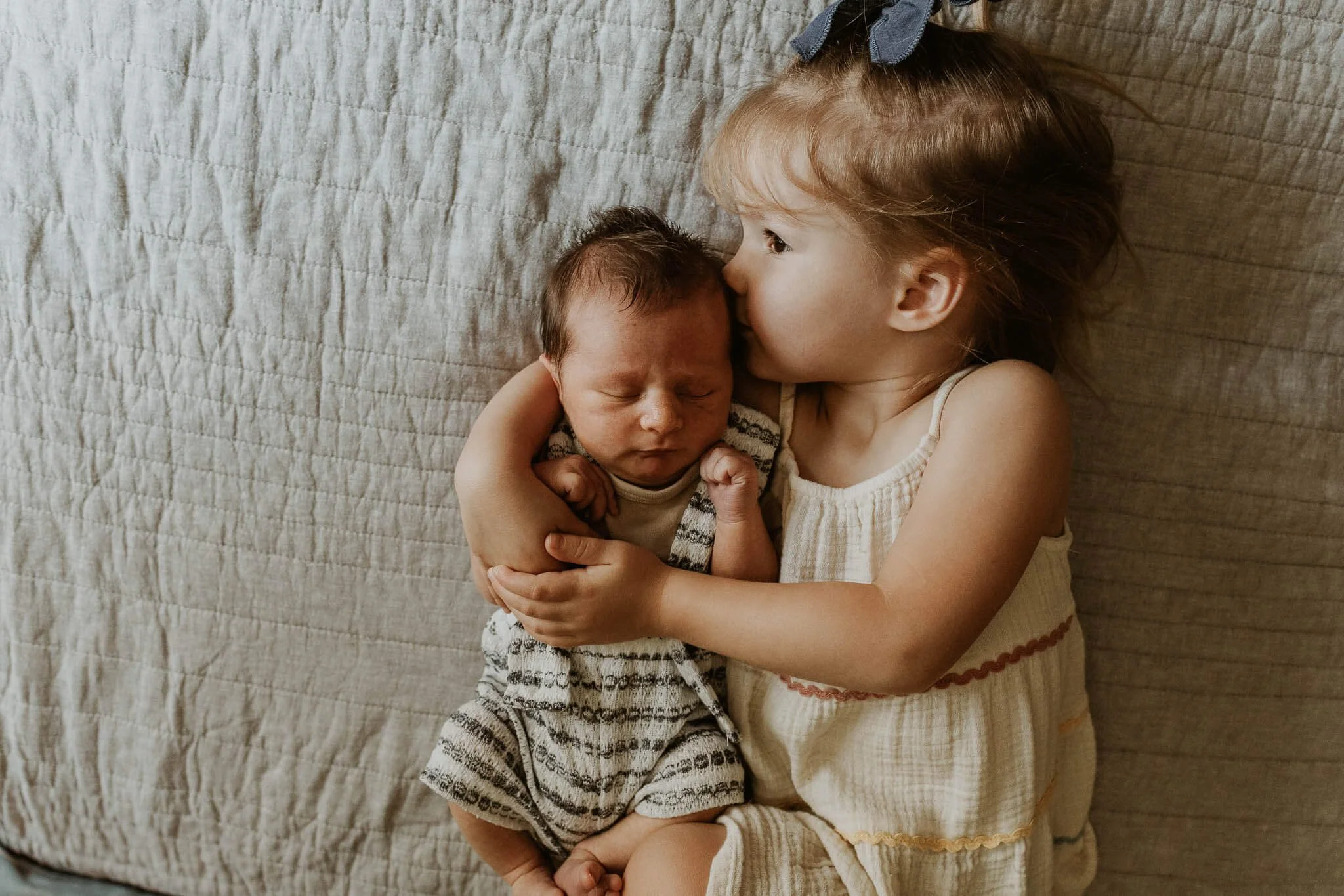Big sister kissing newborn brother during newborn home session.