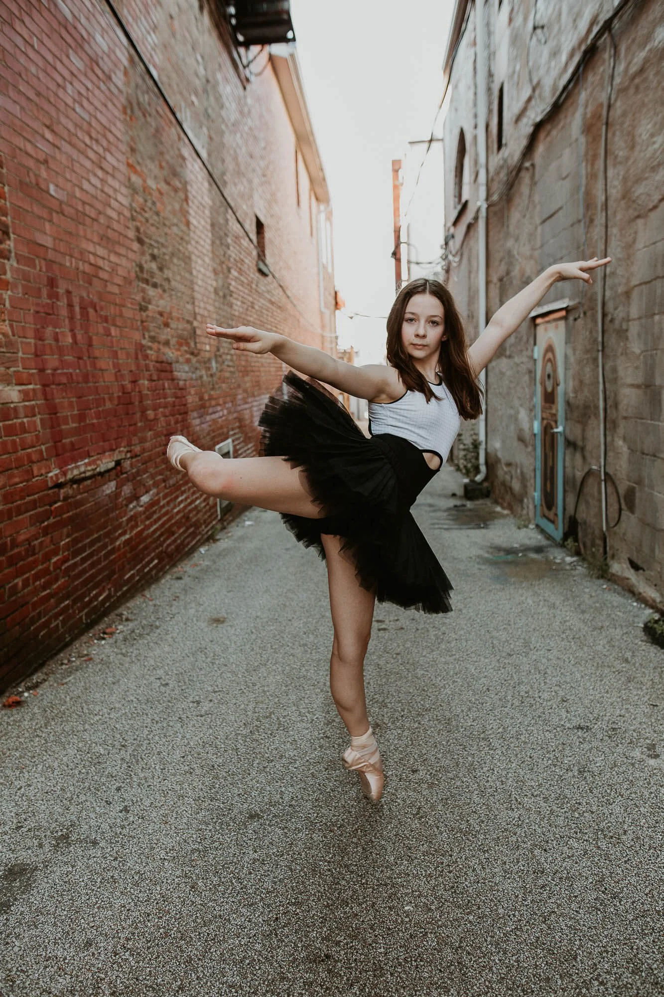 Katie holds herself en pointe, her top leg bent parallel to the ground.