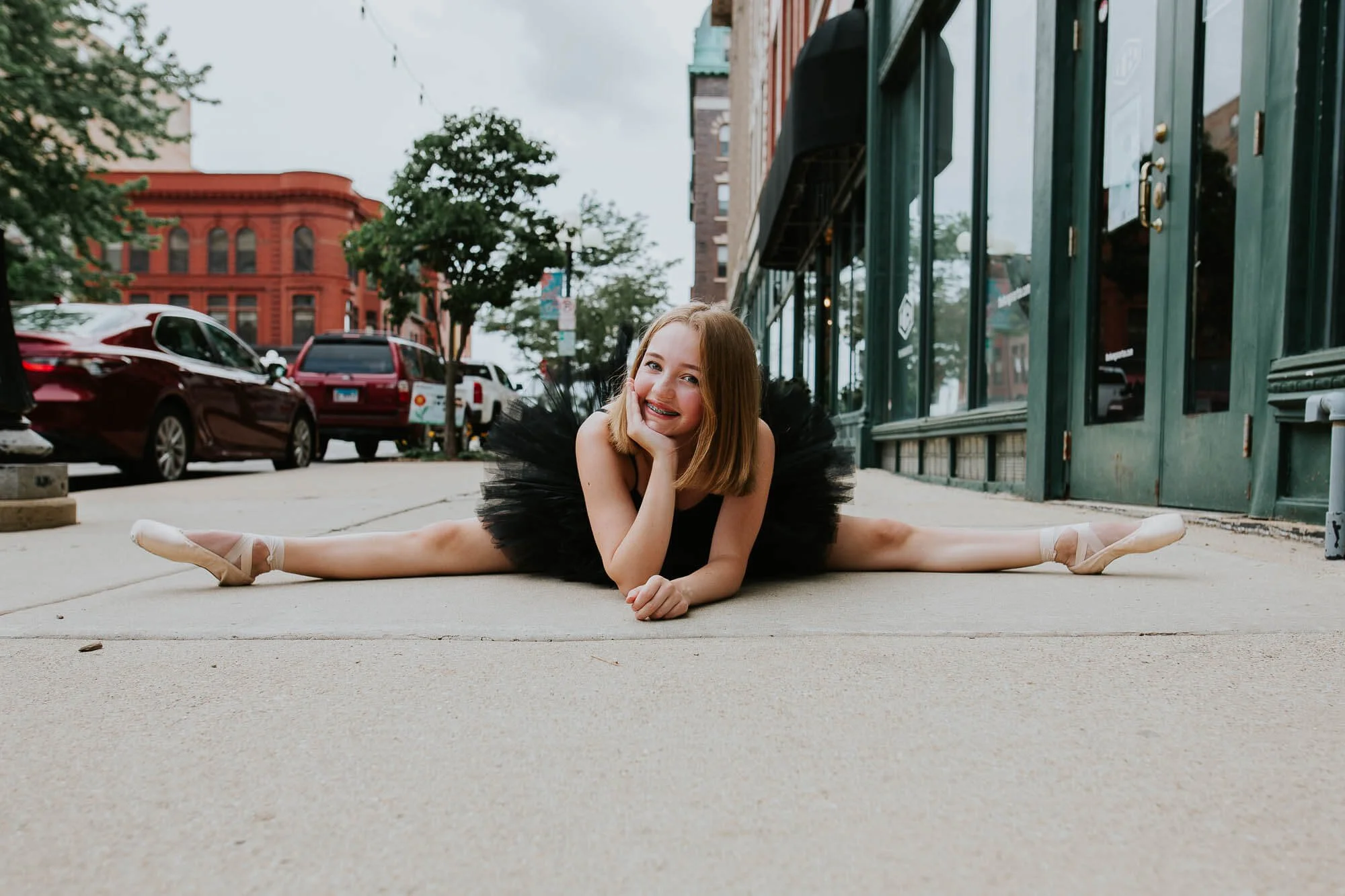 A teenage girl dones a tutu and pointe shoes while in the splits on a sidewalk in Downtown Bloomington IL