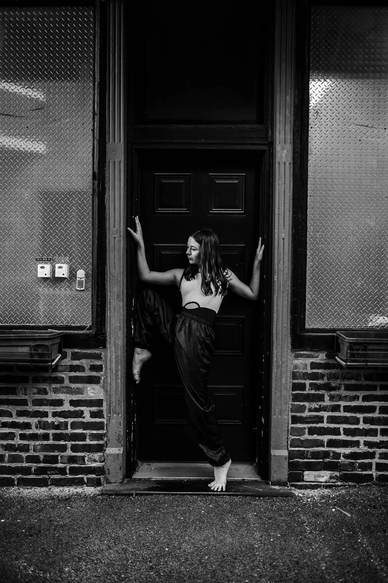 A black and white image of a dancer in a doorway with a funky jazz pose.
