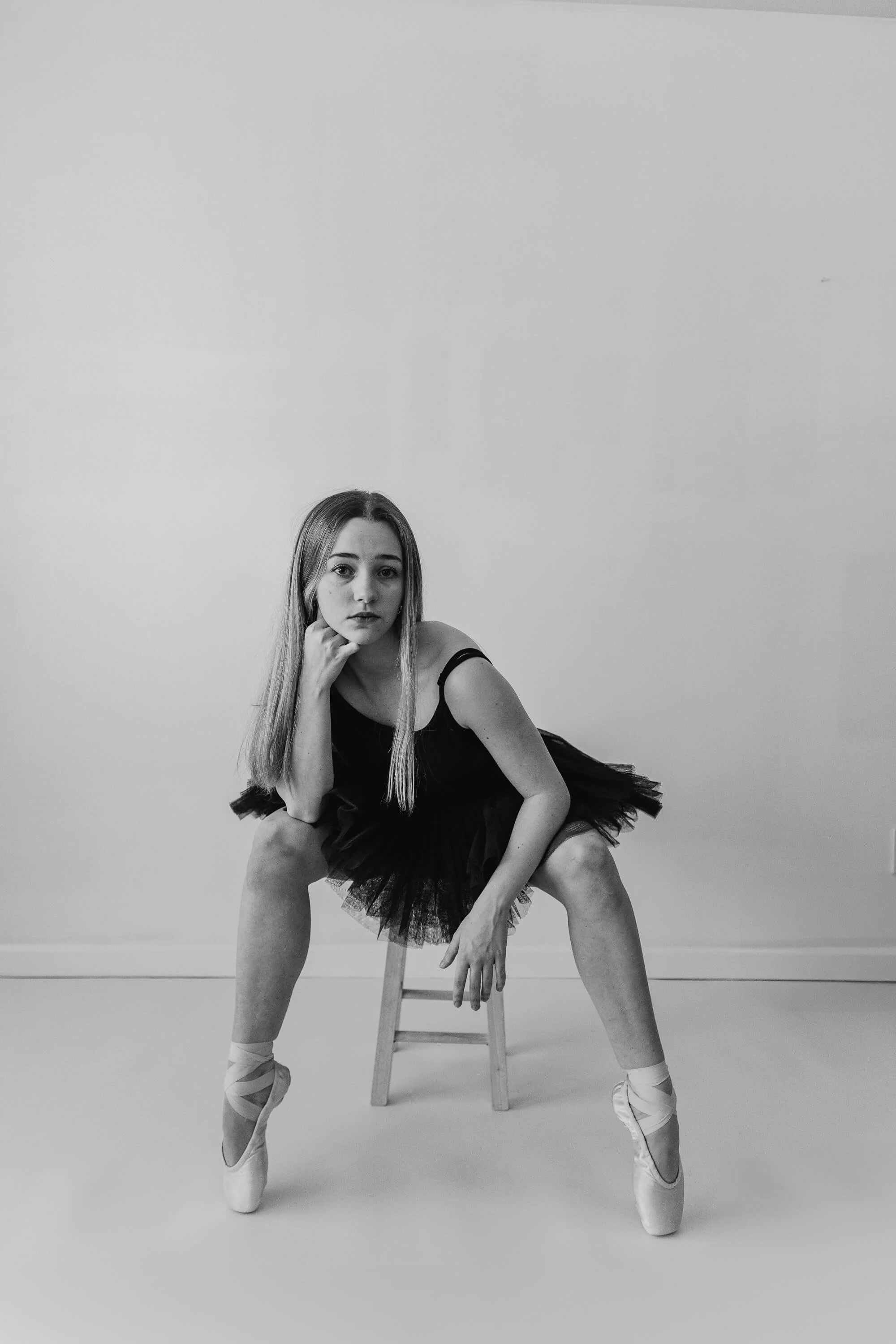 A black and white of a ballet dancer sitting atop a short wooden stool.