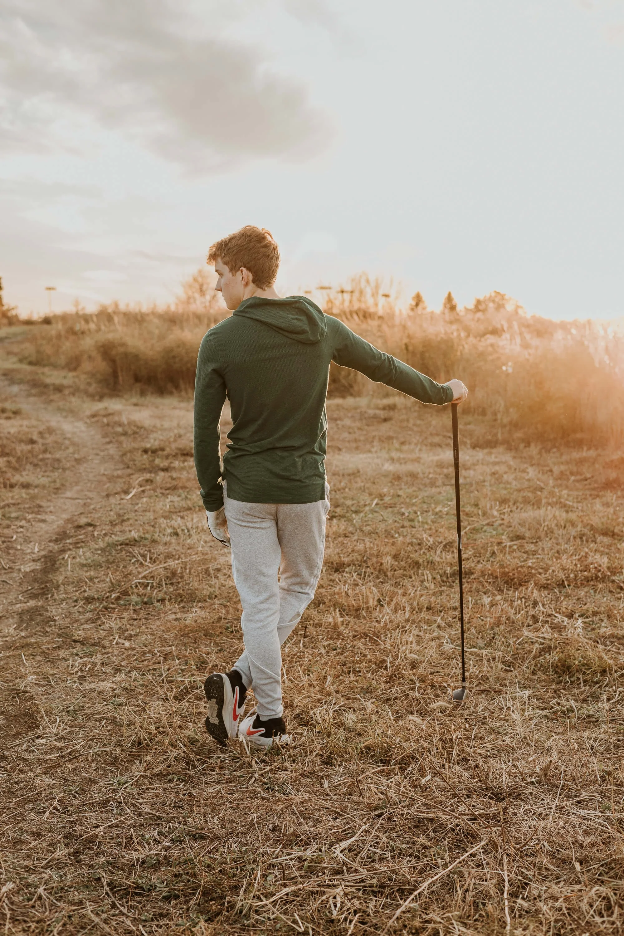 A high school senior holds his golf club at sunset overlooking the green