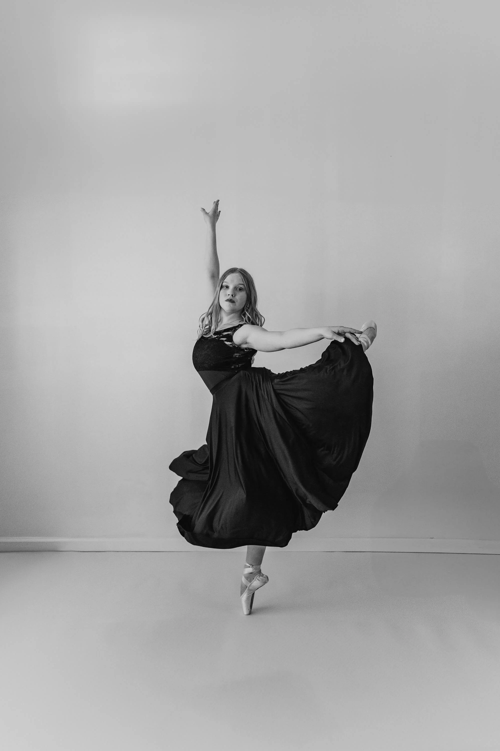 A black and white image of a dancer wearing a flowy skirt, holding a pose en pointe.