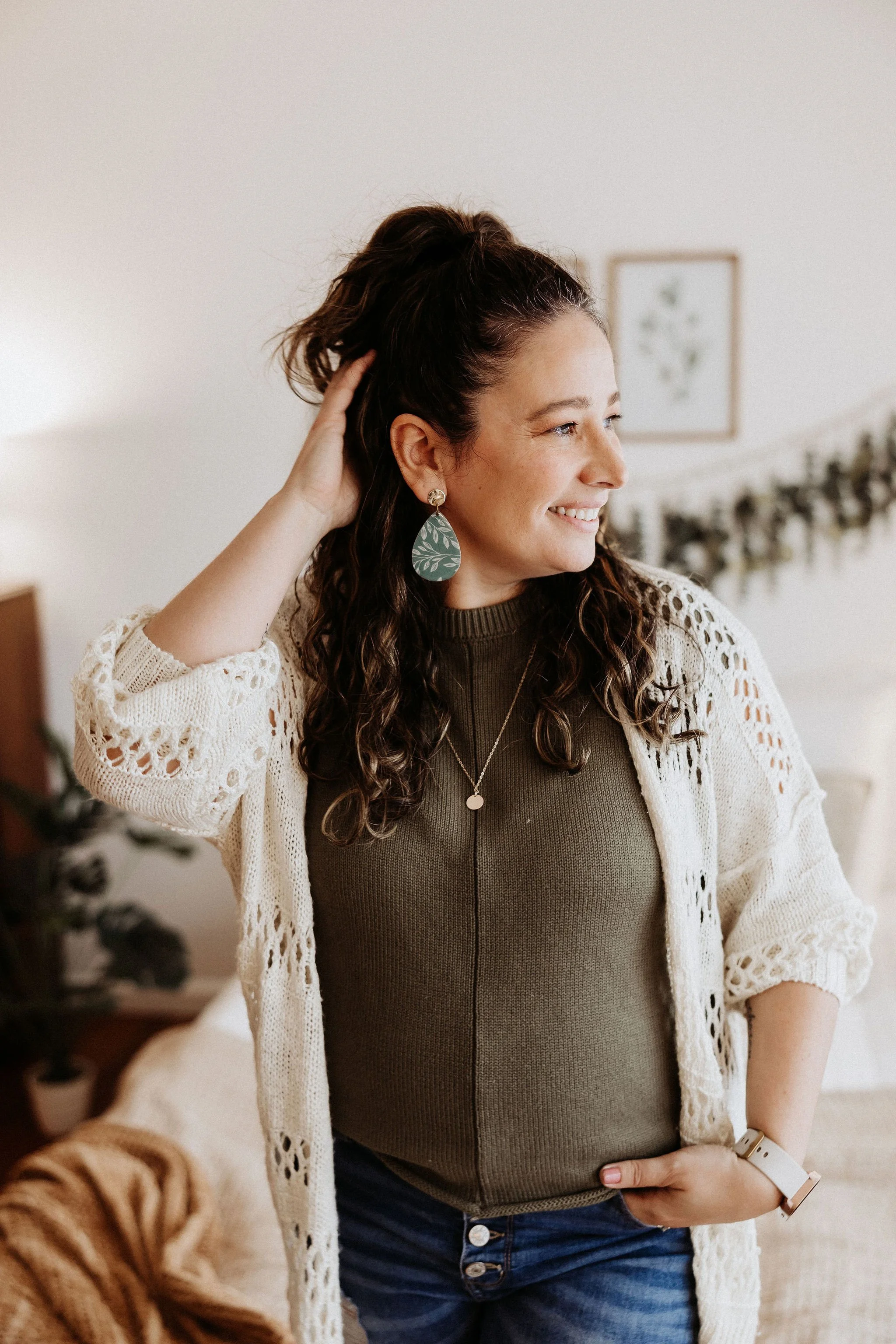 Liz Walsh stands in her studio, hand on head, smiling, looking out the window