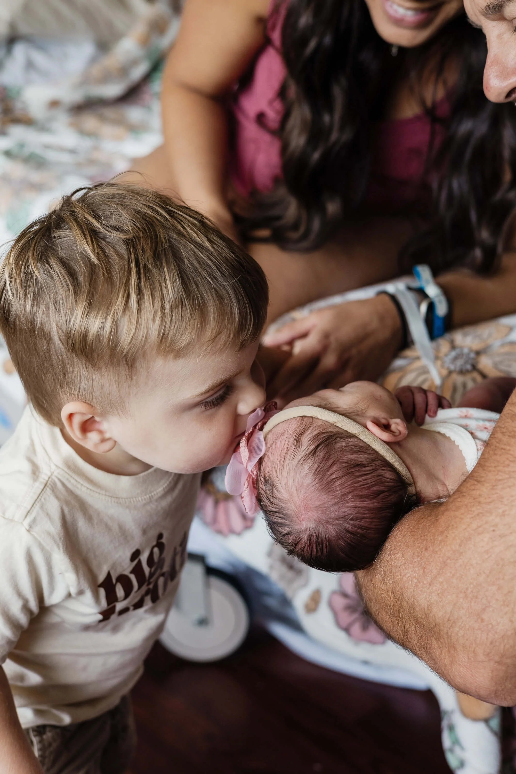 A new big brother, a 2 year old boy sweetly kisses the top of his sister's newborn head