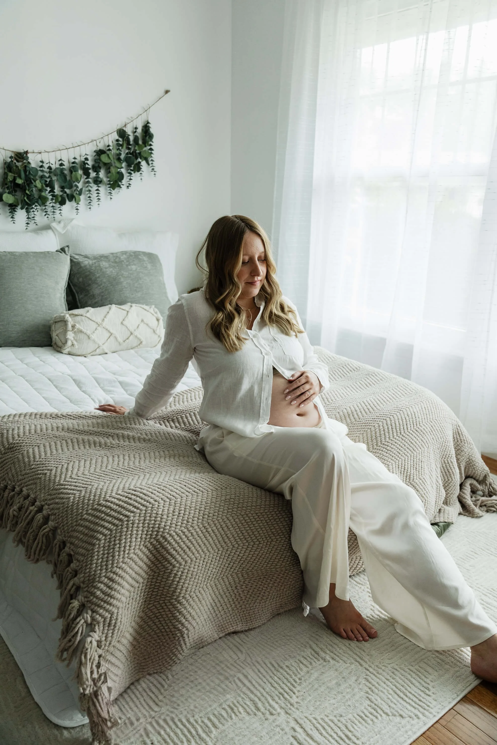 A mom-to-be sits quietly on a bed at Liz Walsh Photography's studio in Bloomington IL