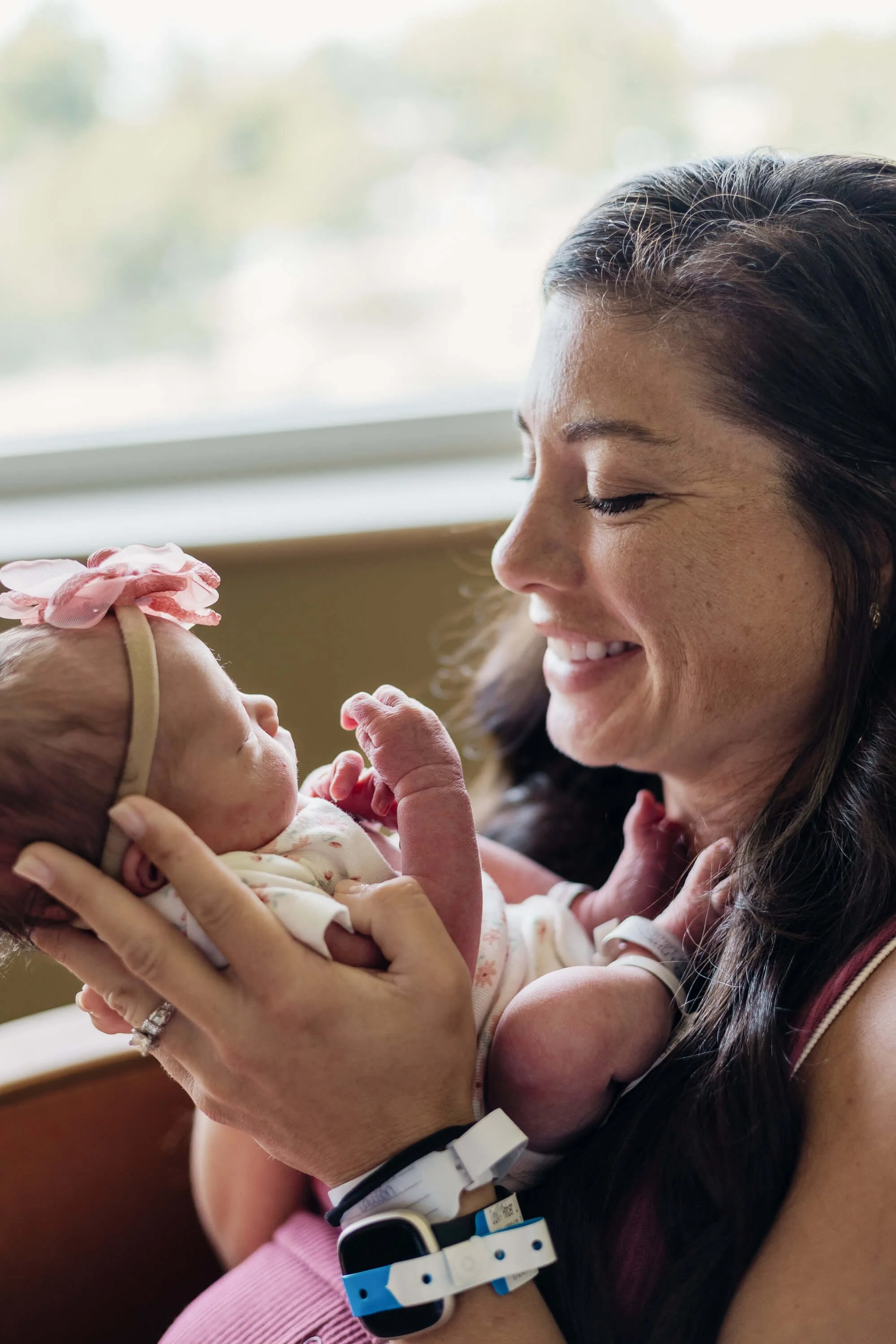 A mother dons her hospital bracelets as she smiles down at her brand new baby girl
