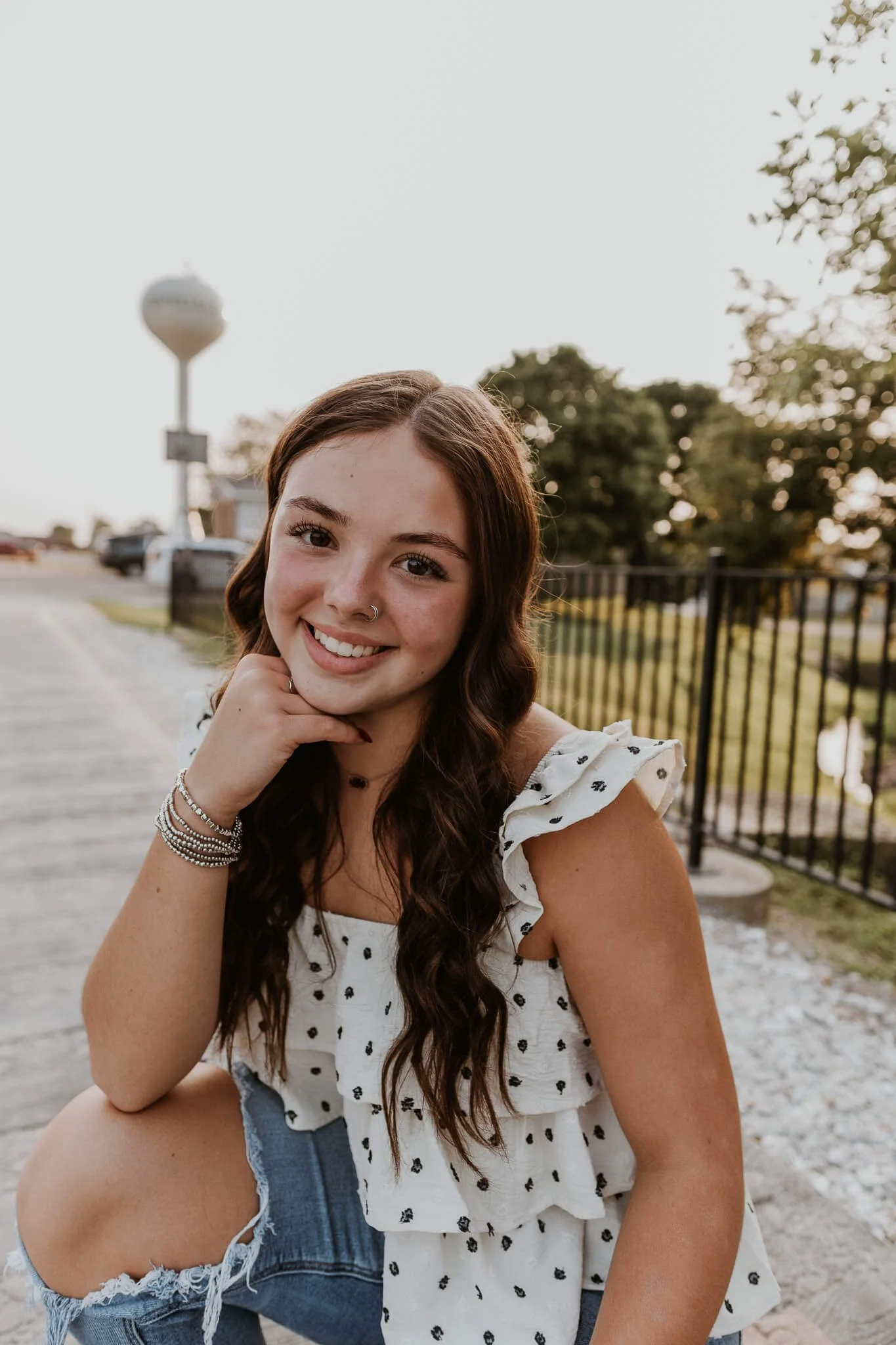 A high school senior kneels on a bridge at the local park near her high school