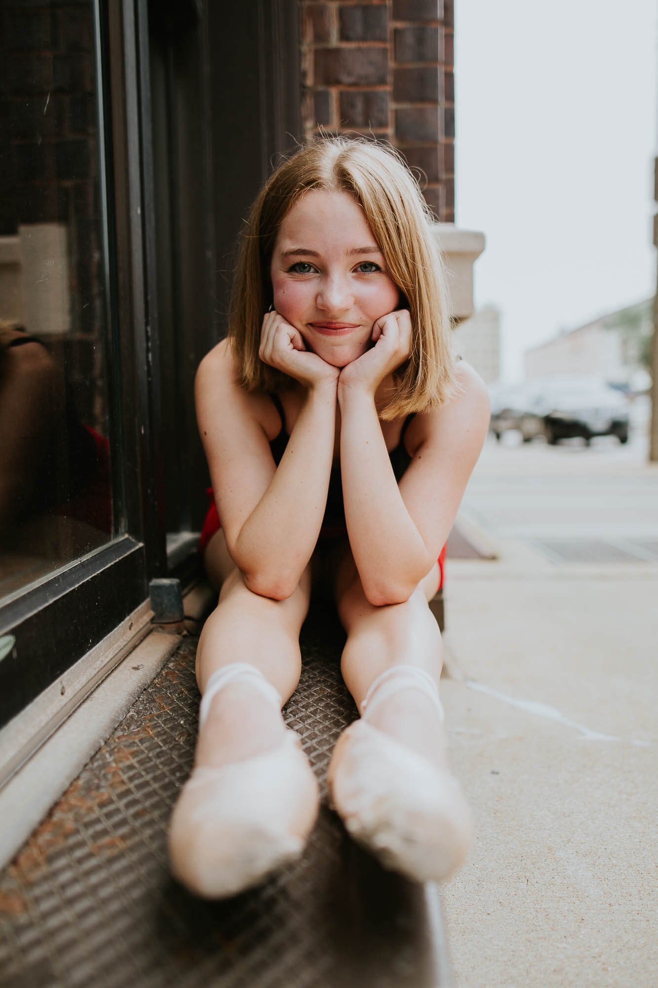A ballerina sits leaning forward, elbows propped on her knees, a soft smile on her face
