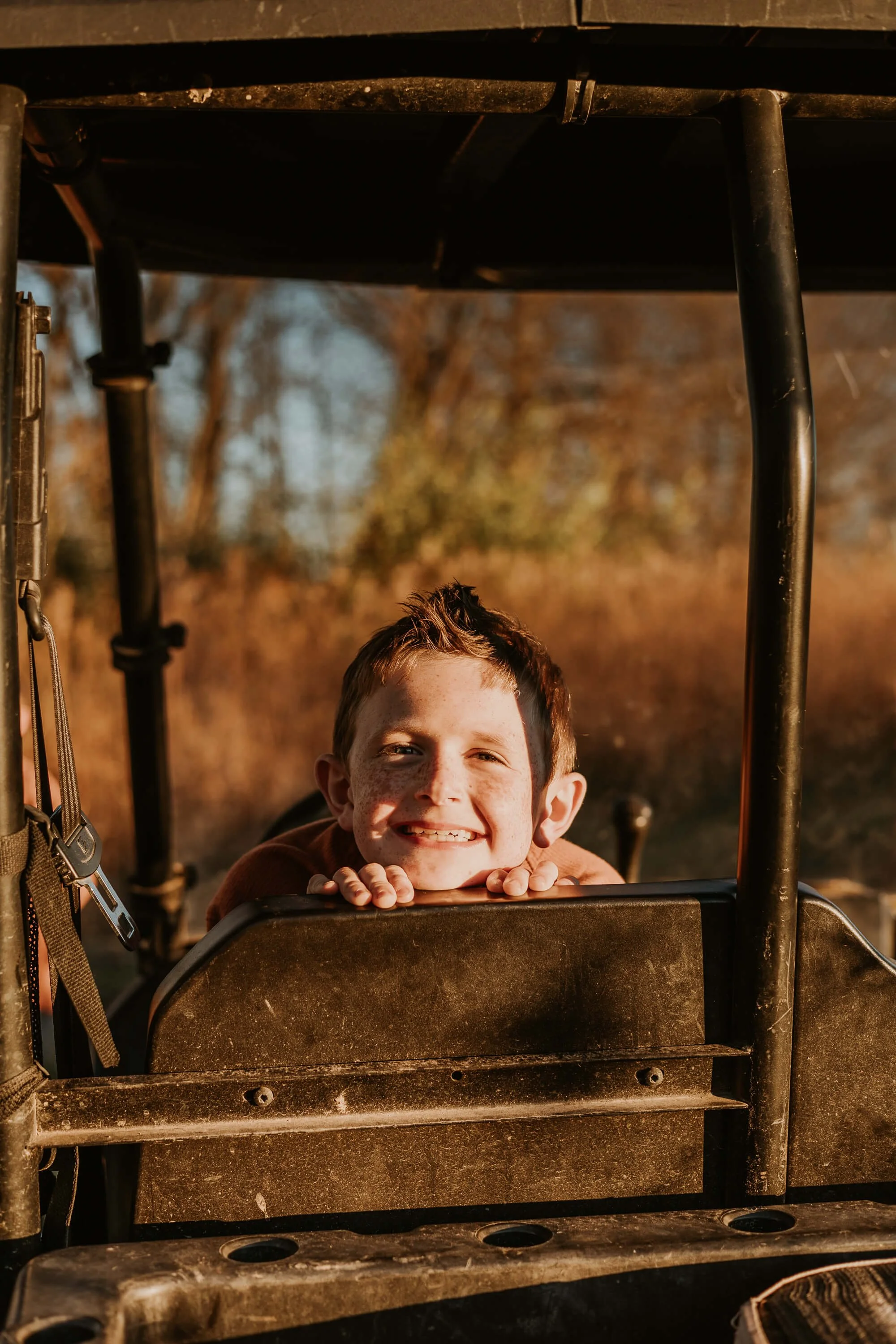 A young boy peeks over the back of a golf cart with a big smile on his face.