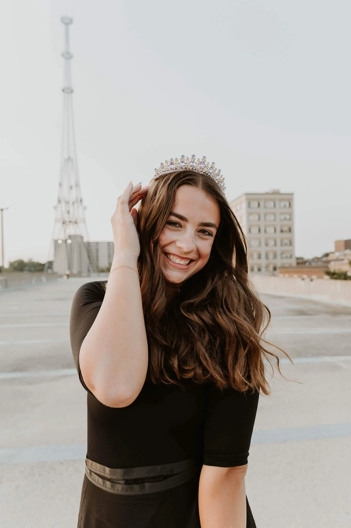 A teen girl smiles widely while tucking hair behind her ear