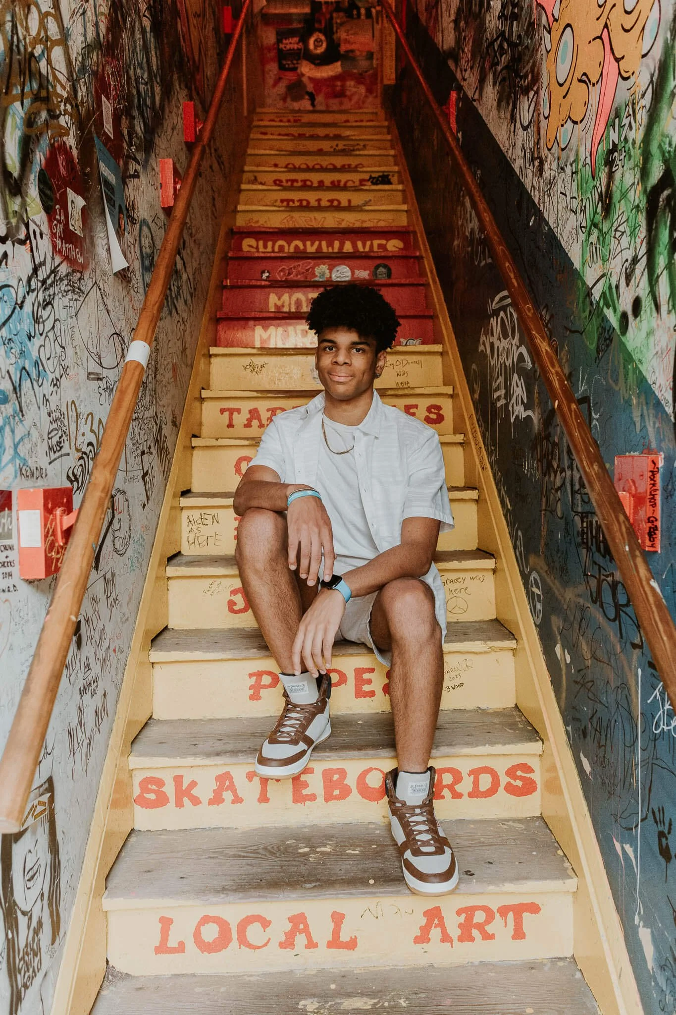 A senior boy sits in the stairwell the leads up to Shockwave Skateboards in Uptown Normal.