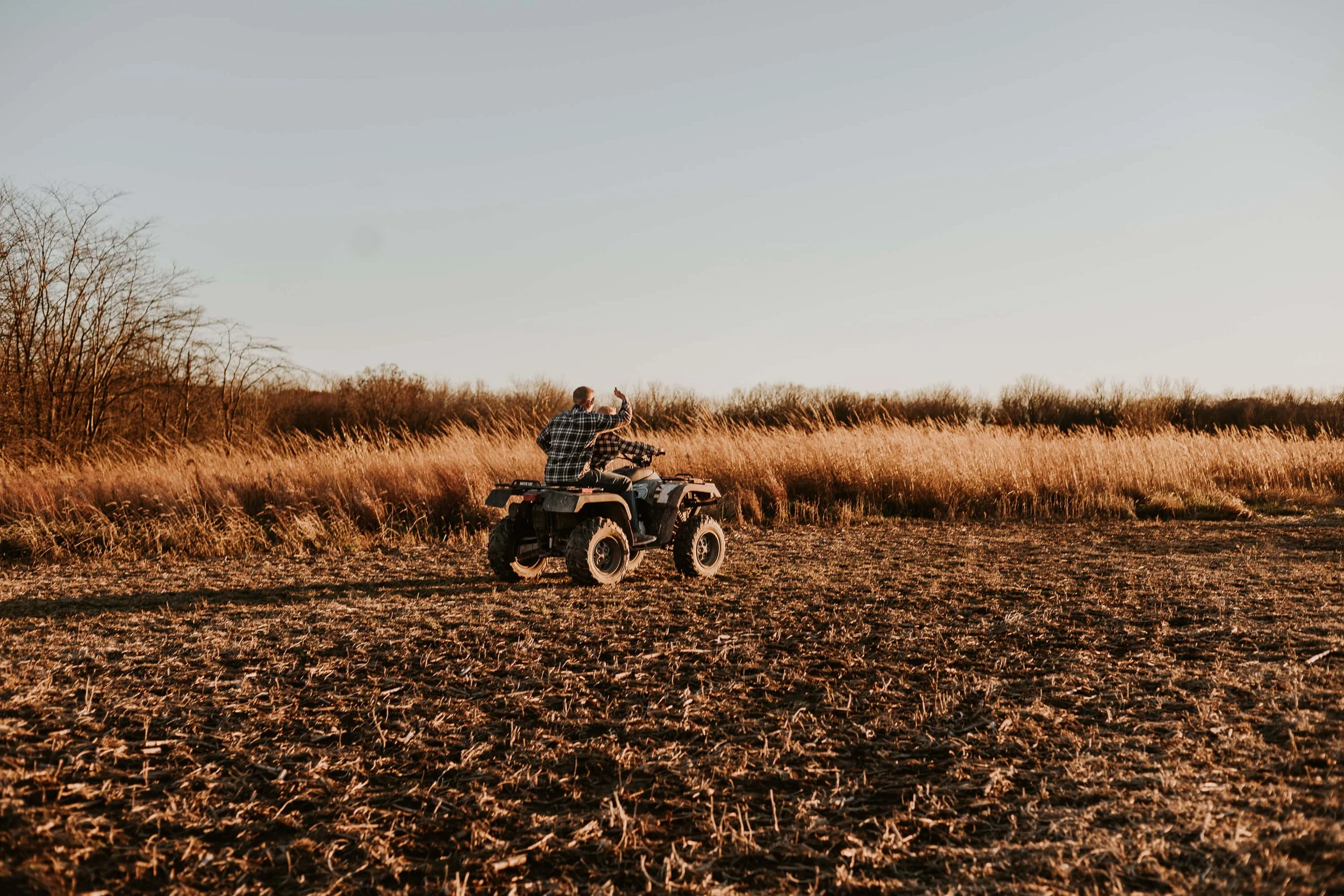A father gives his ten year old son a ride on a four wheeler 