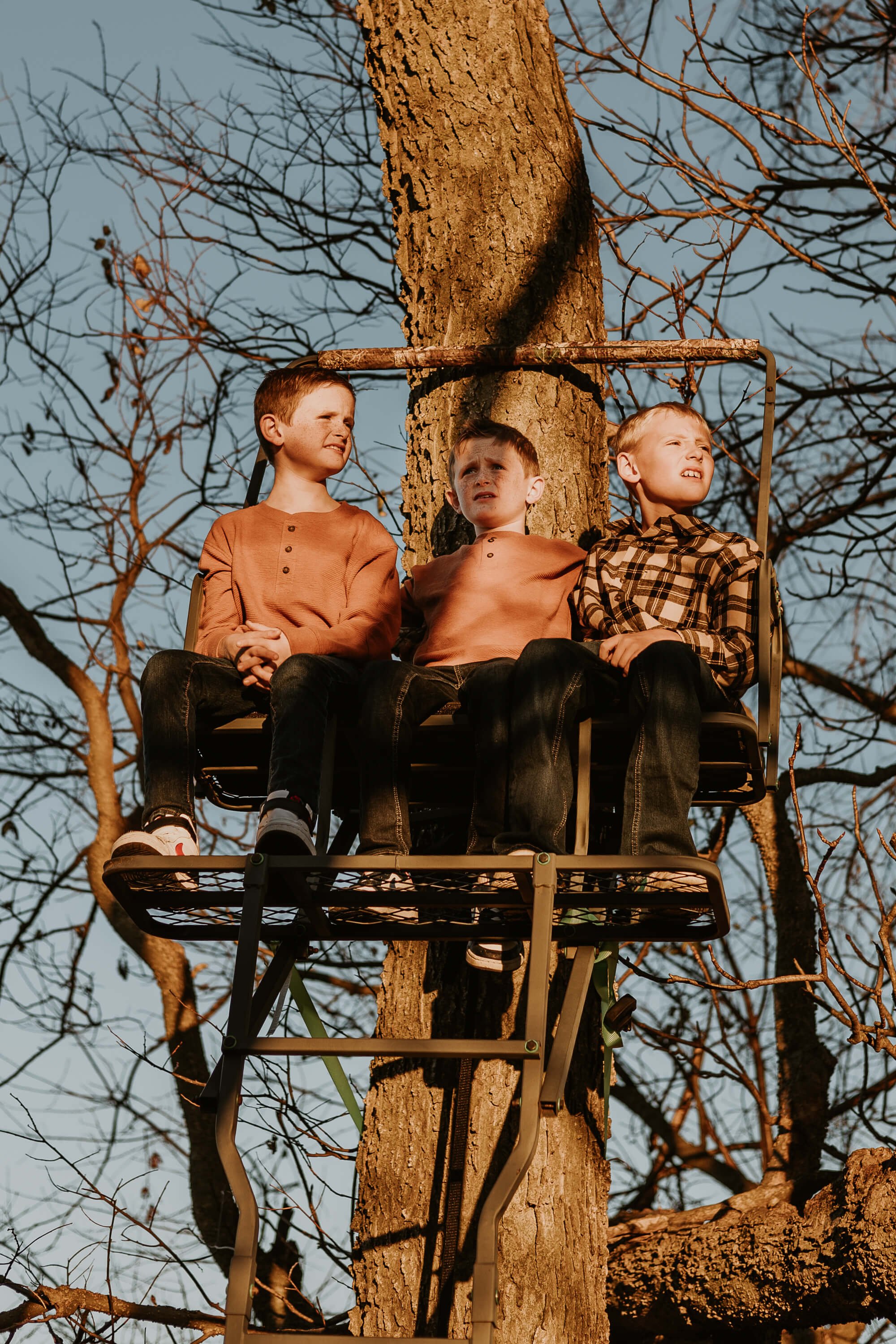 A ten year old boy and his two younger, twin brothers scope out the farmland that surrounds the deer stand they're in