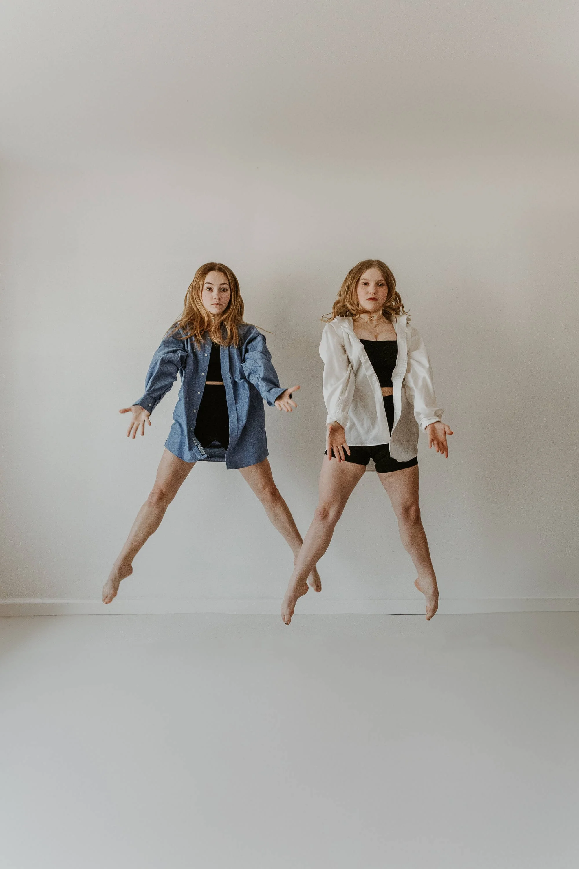 Two dancers wearing oversized men's dress shirts, jump in tandem.