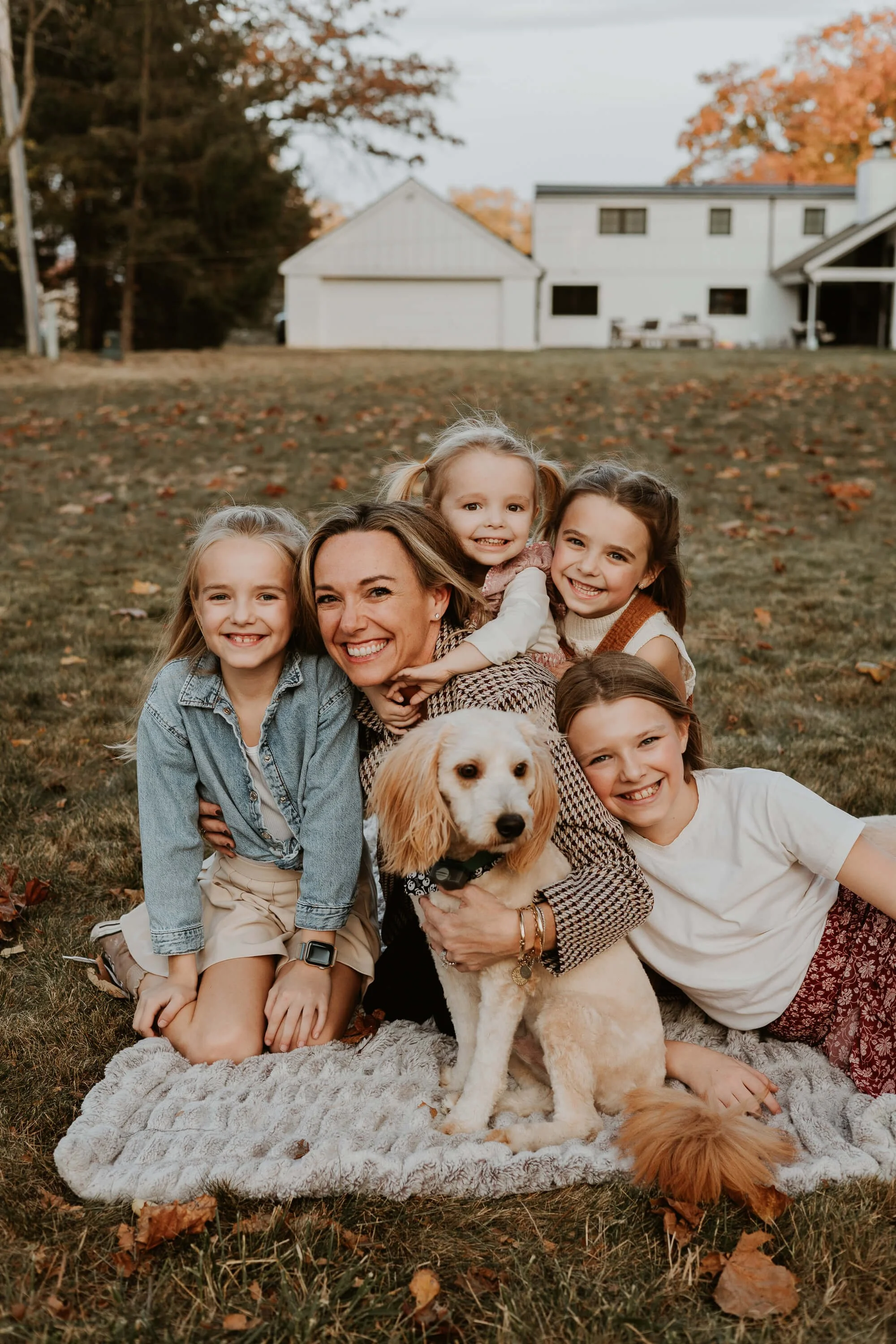 A mom and her four daughters along with their puppy giggle on a blanket in their backyard