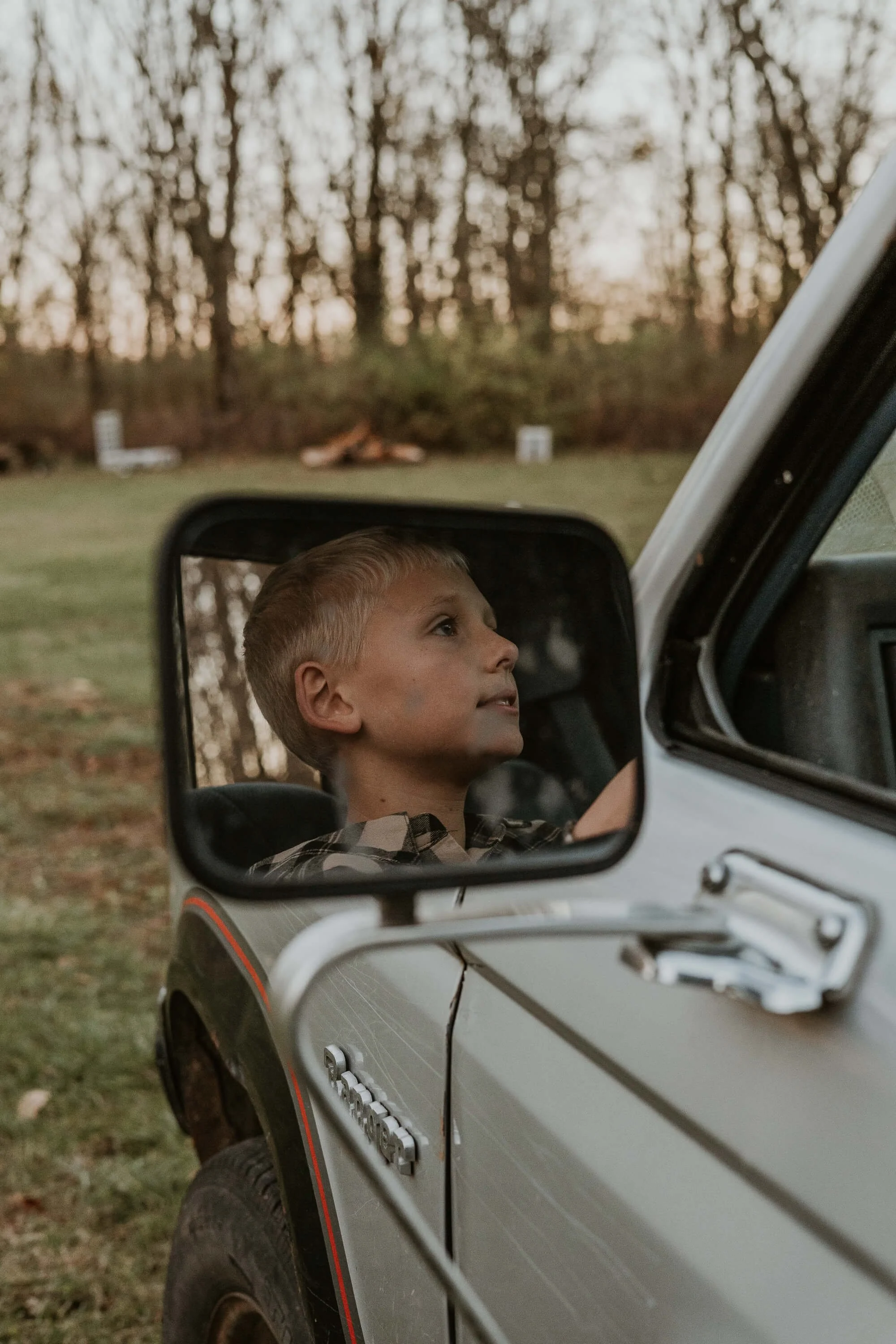 A reflection of a boy from the side mirror of a pick up truck