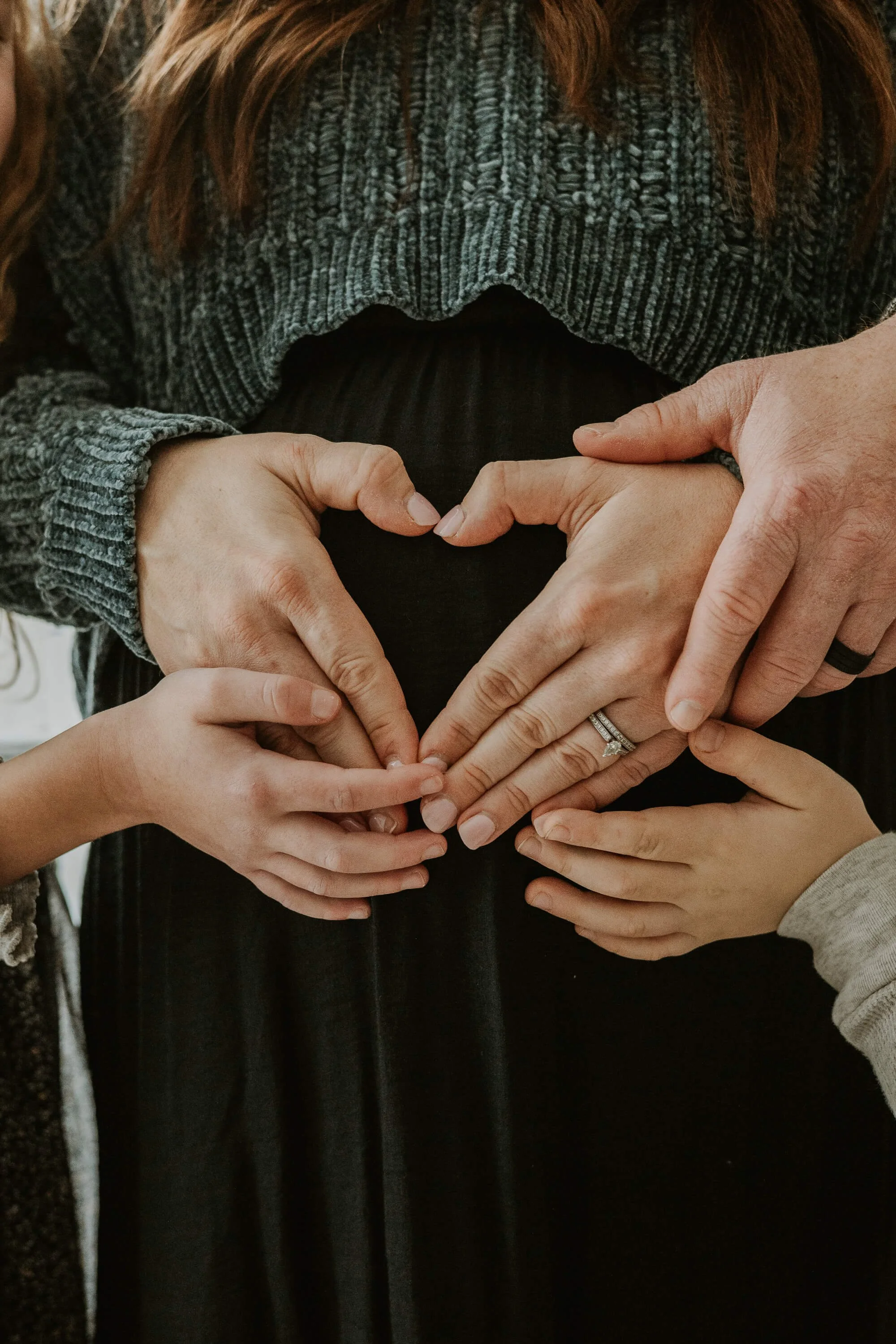 A close up shot of a pregnant belly with four sets of hands gently touching the belly