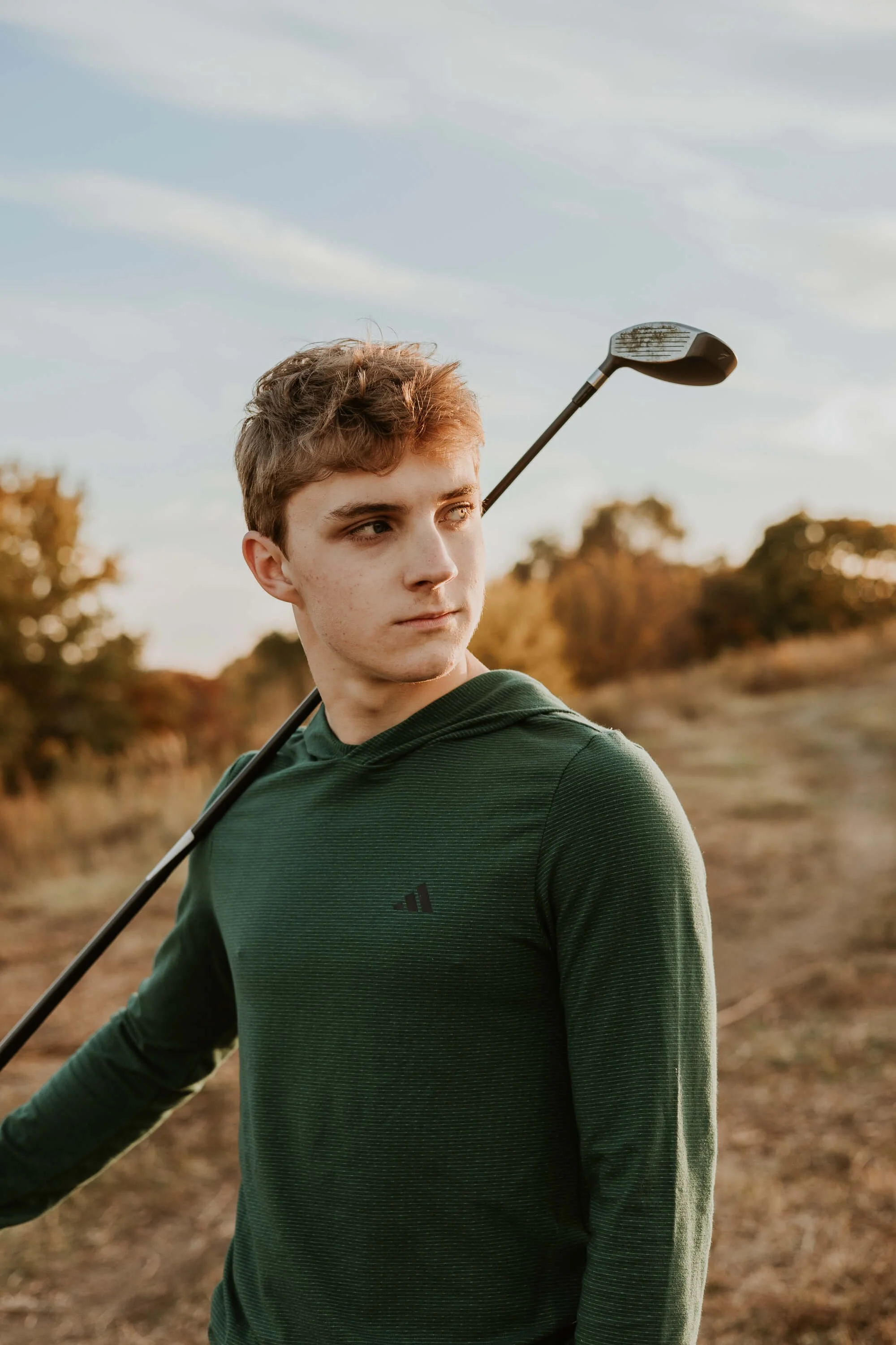 A portrait of a high school senior boy holding his golf club informally over his shoulder