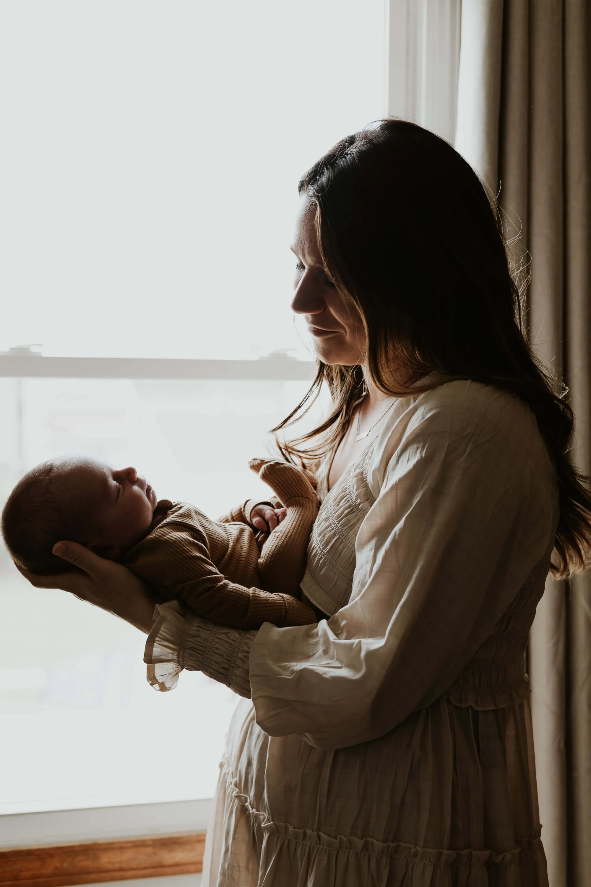 A sillhouette of a mother looking down at her sleeping infant