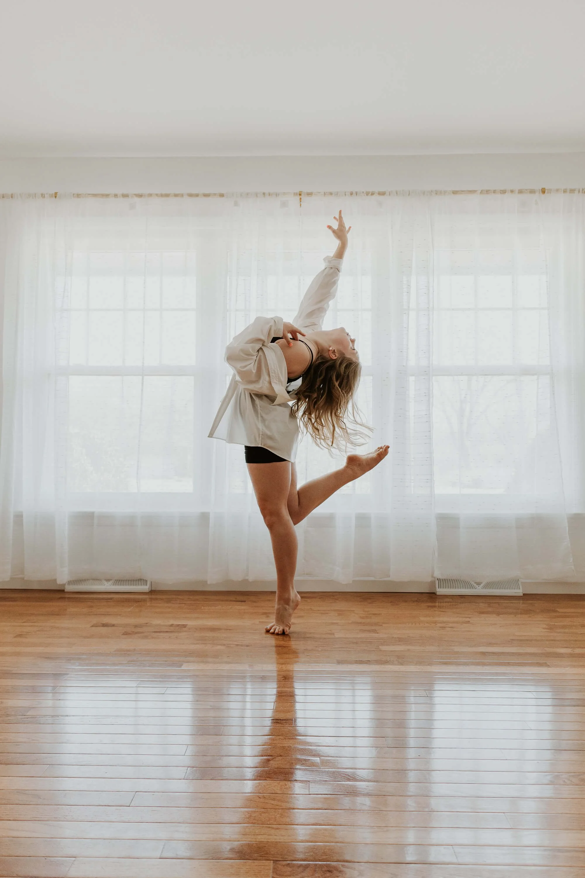 A dancer on tip toe balances on one foot and bends her other leg backwards towards the ceiling.