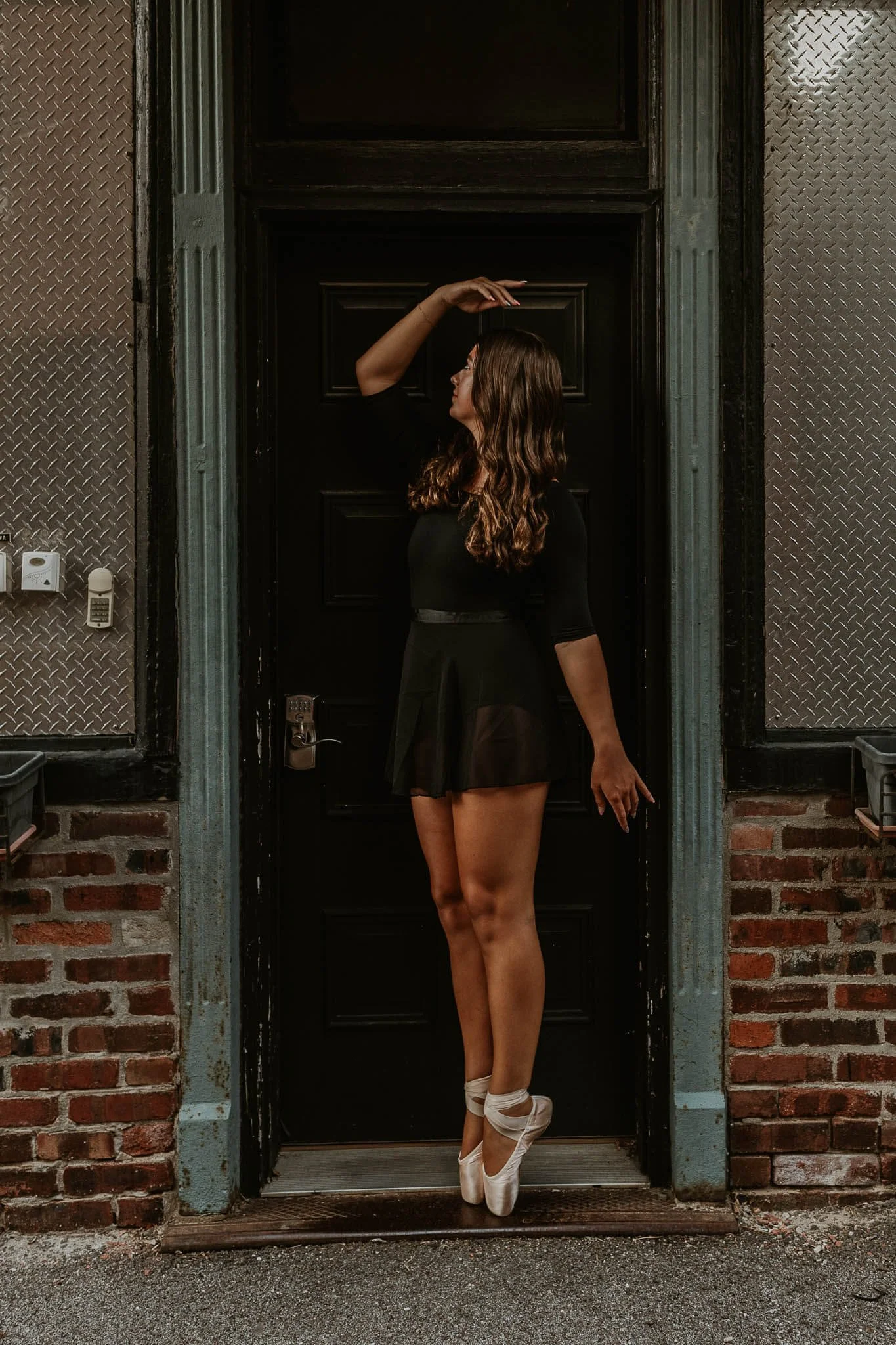 En pointe framed by a doorway, a ballerina holds her arm gracefully above her head