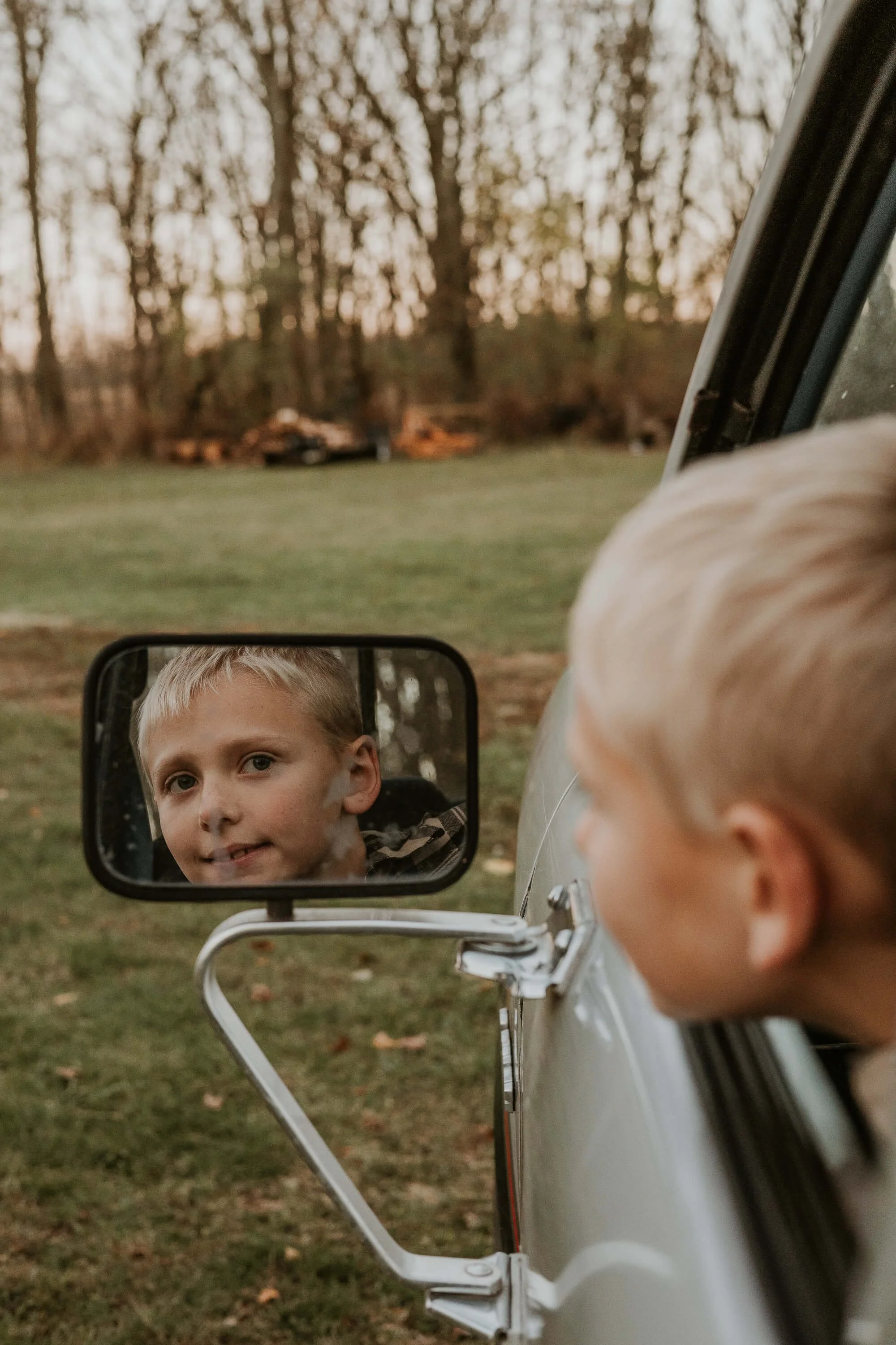 A young boy looks out the window of a beat up truck, his reflection showing the glee on his face as he pretends to drive