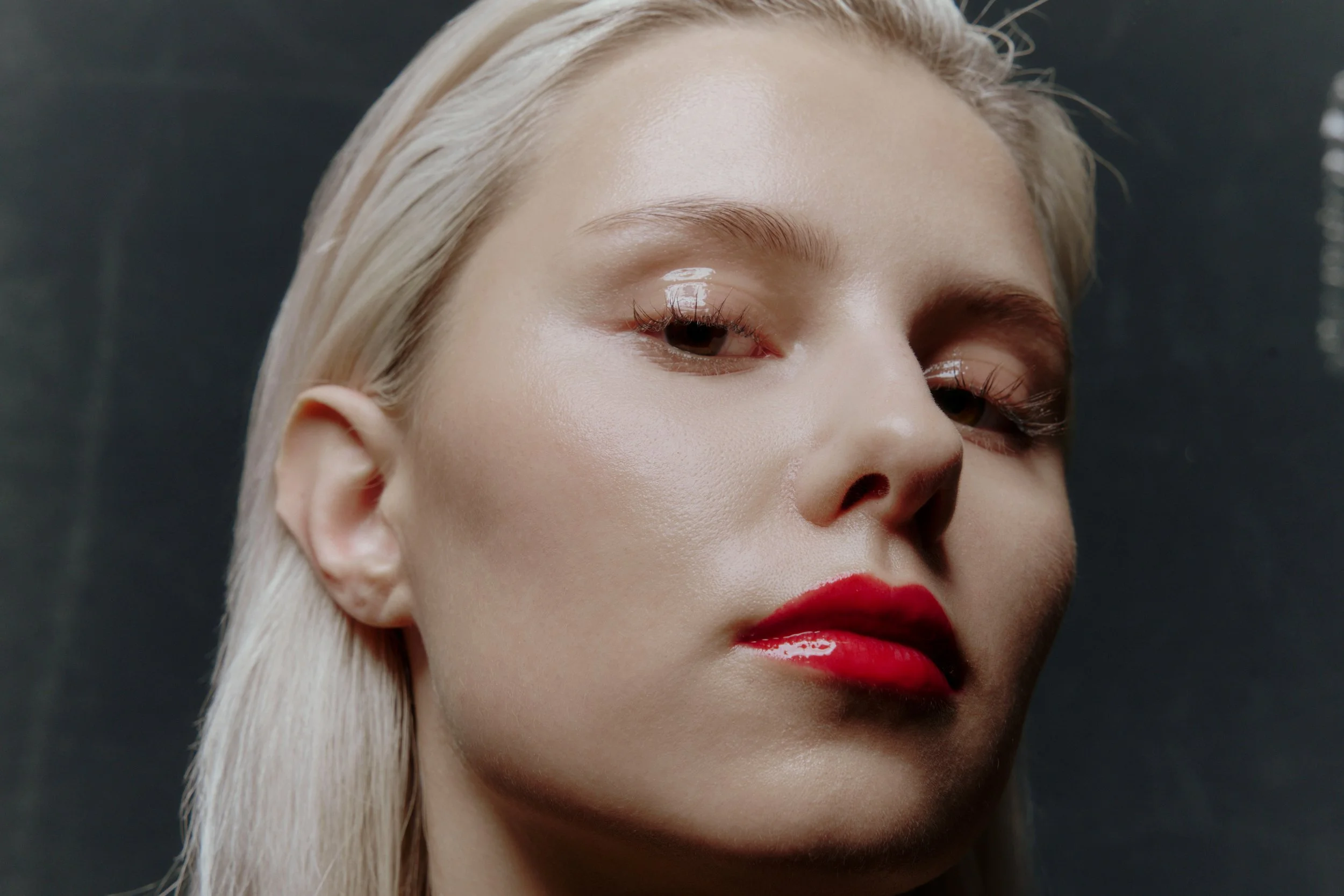 Nahaufnahme eines Gesichts einer Frau mit blonden Haaren, rotem Lippenstift und leicht geröteten Augenlidern.