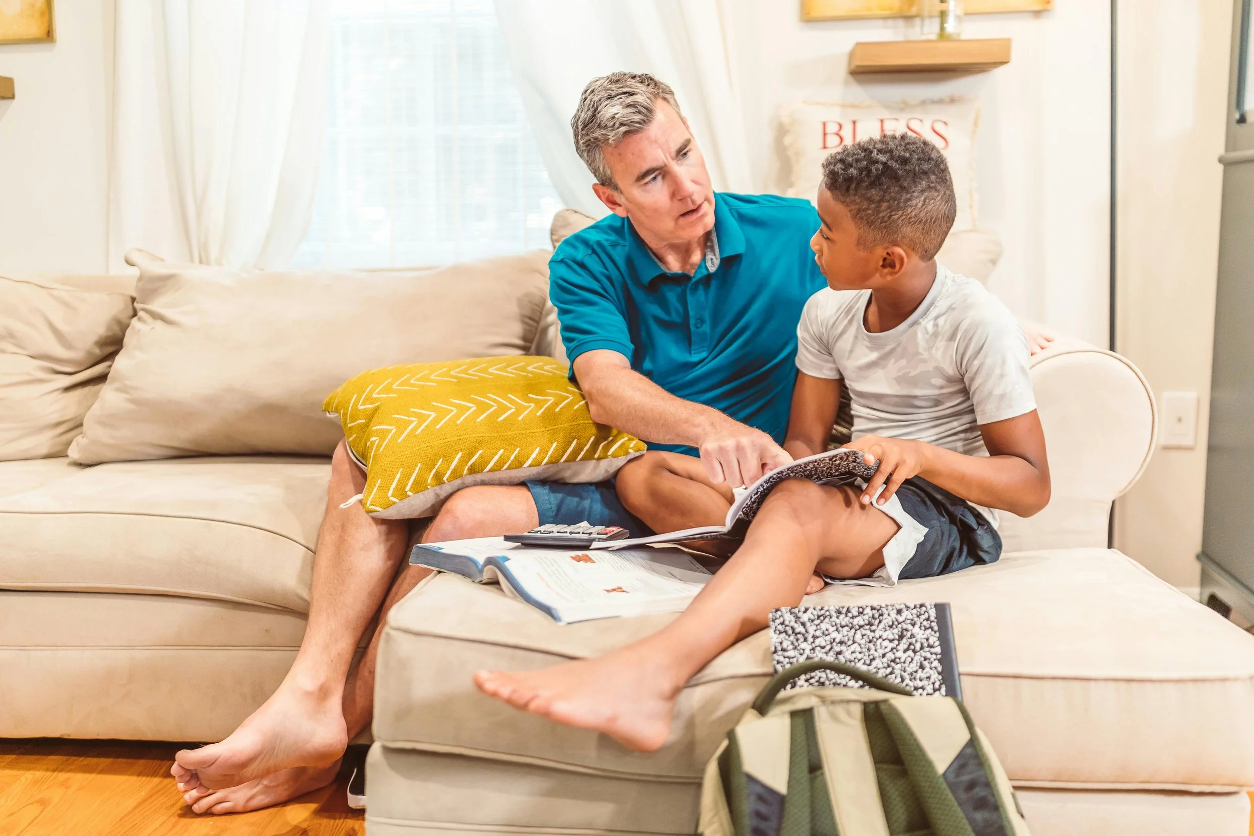 Man and child sit on sofa looking at books together.