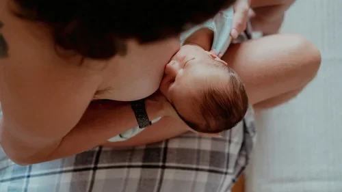 A view from above of a baby with dark hair being breastfed
