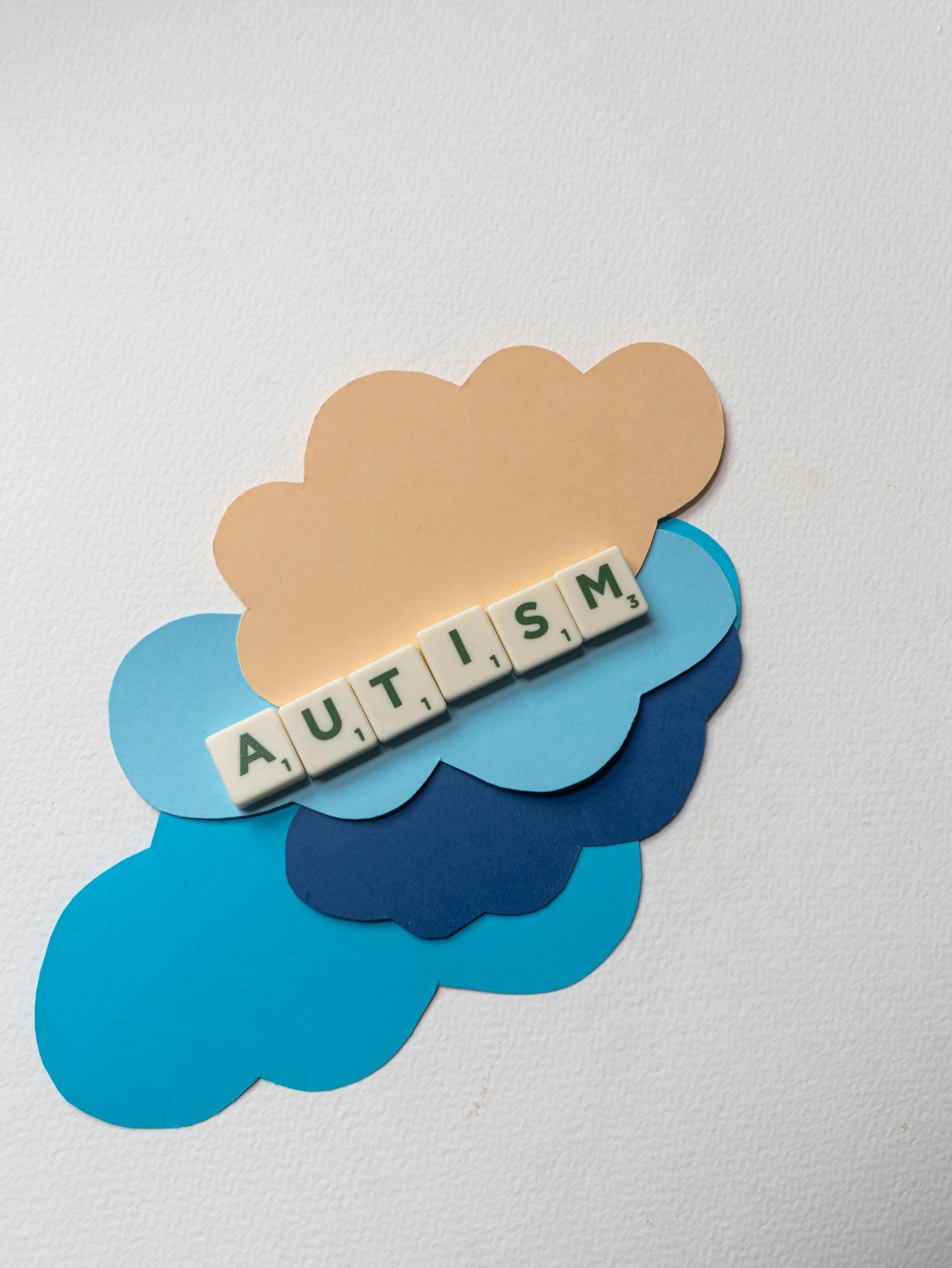 Speech bubbles in cream and blue and scrabble tiles spelling out 'AUTISM'