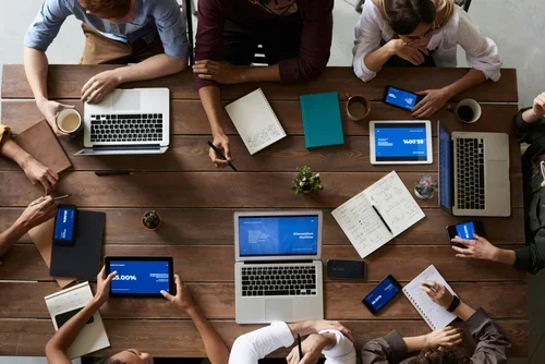 Top down view of people sat around a table with laptops and note pads.