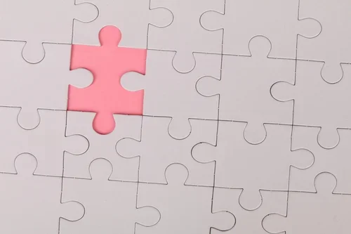 A white jigsaw missing one piece, exposing a red background.