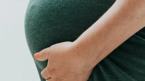 Hand with orange painted nails on a pregnant "bump" wearing a black top.
