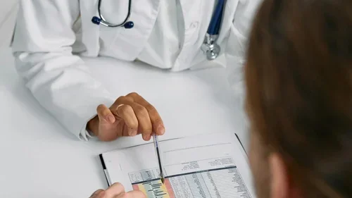 Person in white coat and patient looking at paperwork together