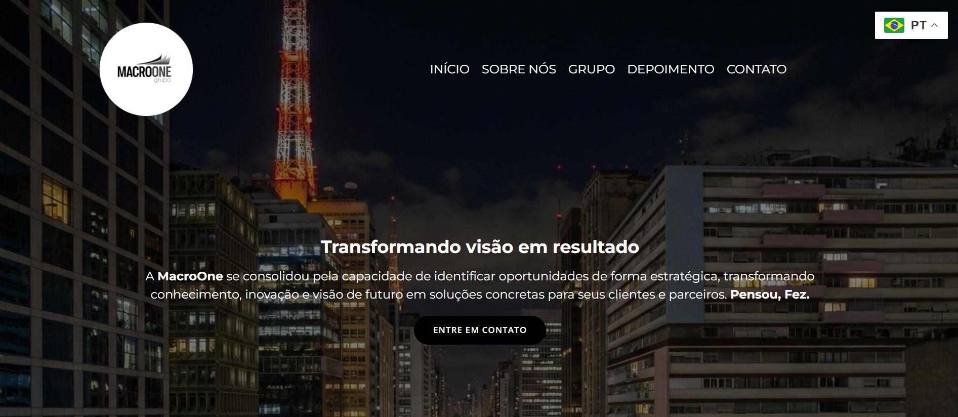 Imagem de uma vista noturna de uma cidade com prédios altos iluminados e uma torre com uma antena vermelha ao fundo, com o site de uma empresa de consultoria chamado MacroOne ao centro.