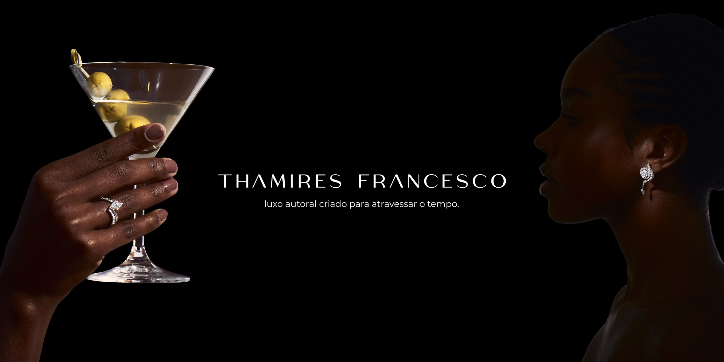 Homem segurando uma taça de coquetel com a mão, usando jóias elegantes, com uma mulher de perfil ao fundo contra um fundo preto.