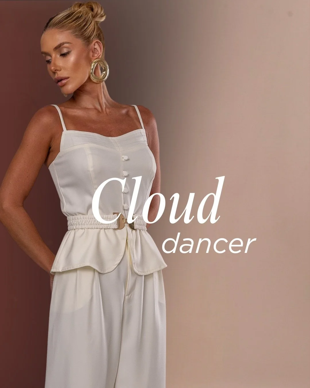 Mulher com cabelo loiro preso, usando brincos de argola grandes, veste blusa branca de alças finas e calça de cintura alta, com o texto 'Cloud dancer' na frente.